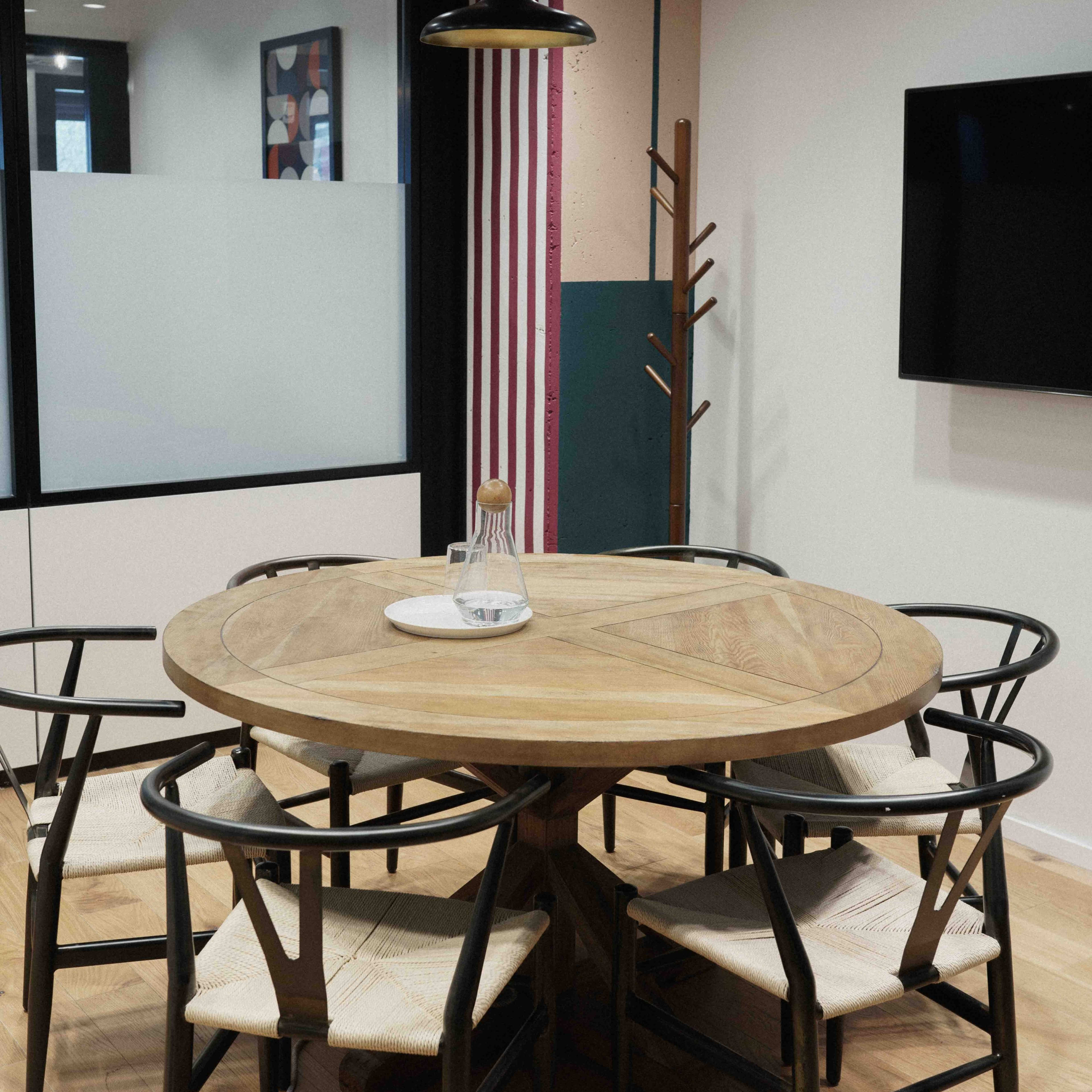 A round wooden dining table surrounded by six black and beige chairs in a modern office setting.