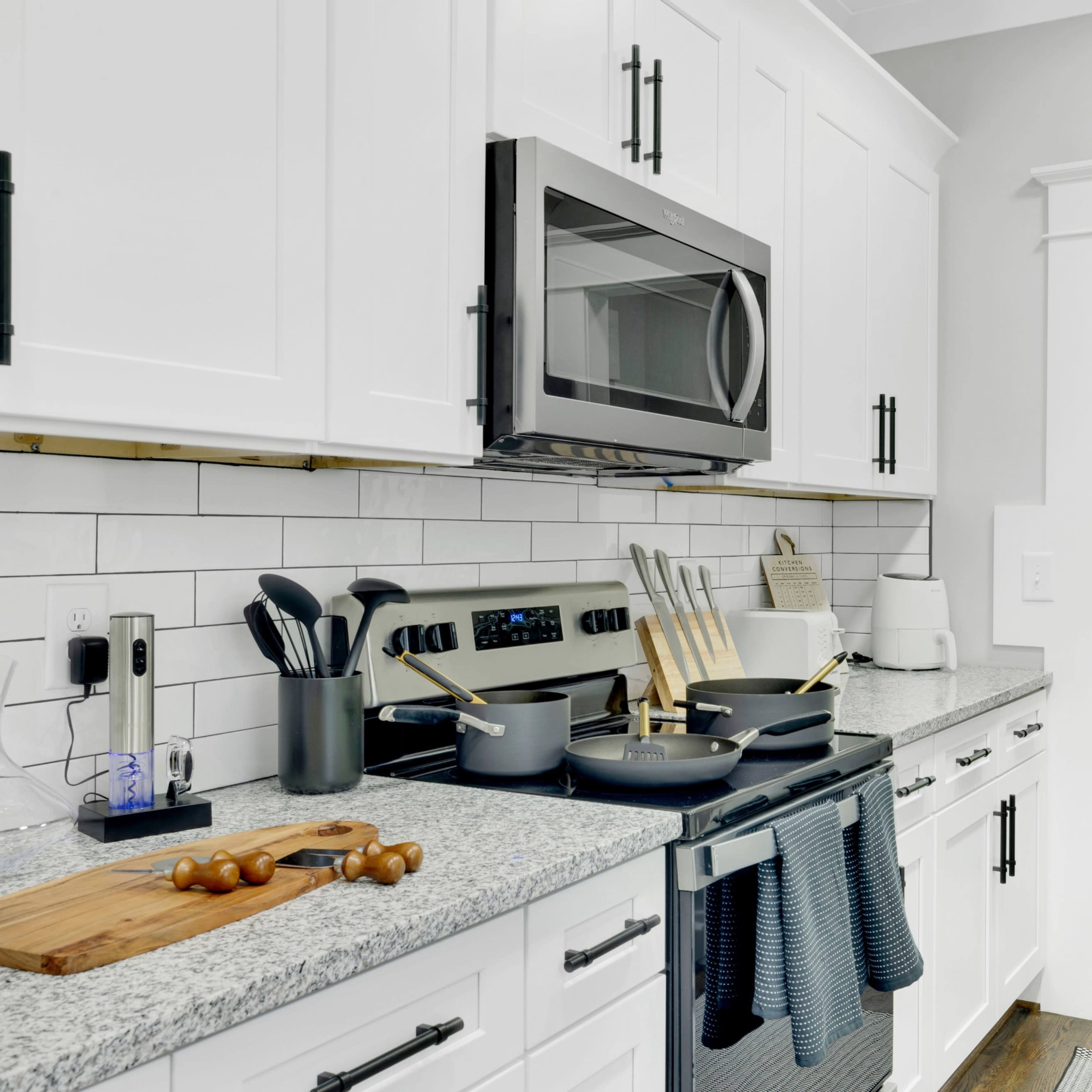 A modern kitchen features white cabinetry, stainless steel appliances, and a wooden door leading outside.
