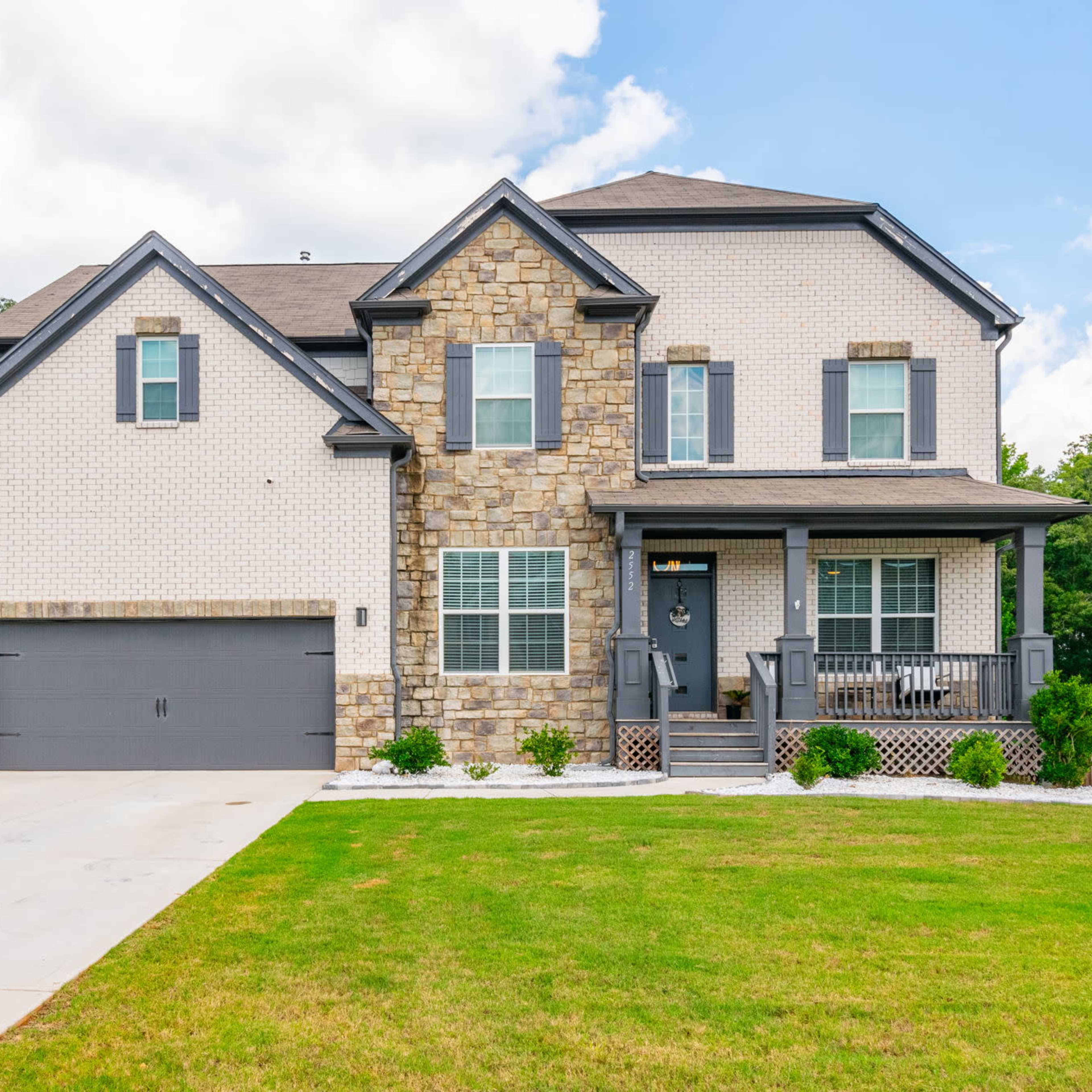 A two-story house with a stone and brick exterior, a front porch, and a double garage is situated on a well-maintained lawn.