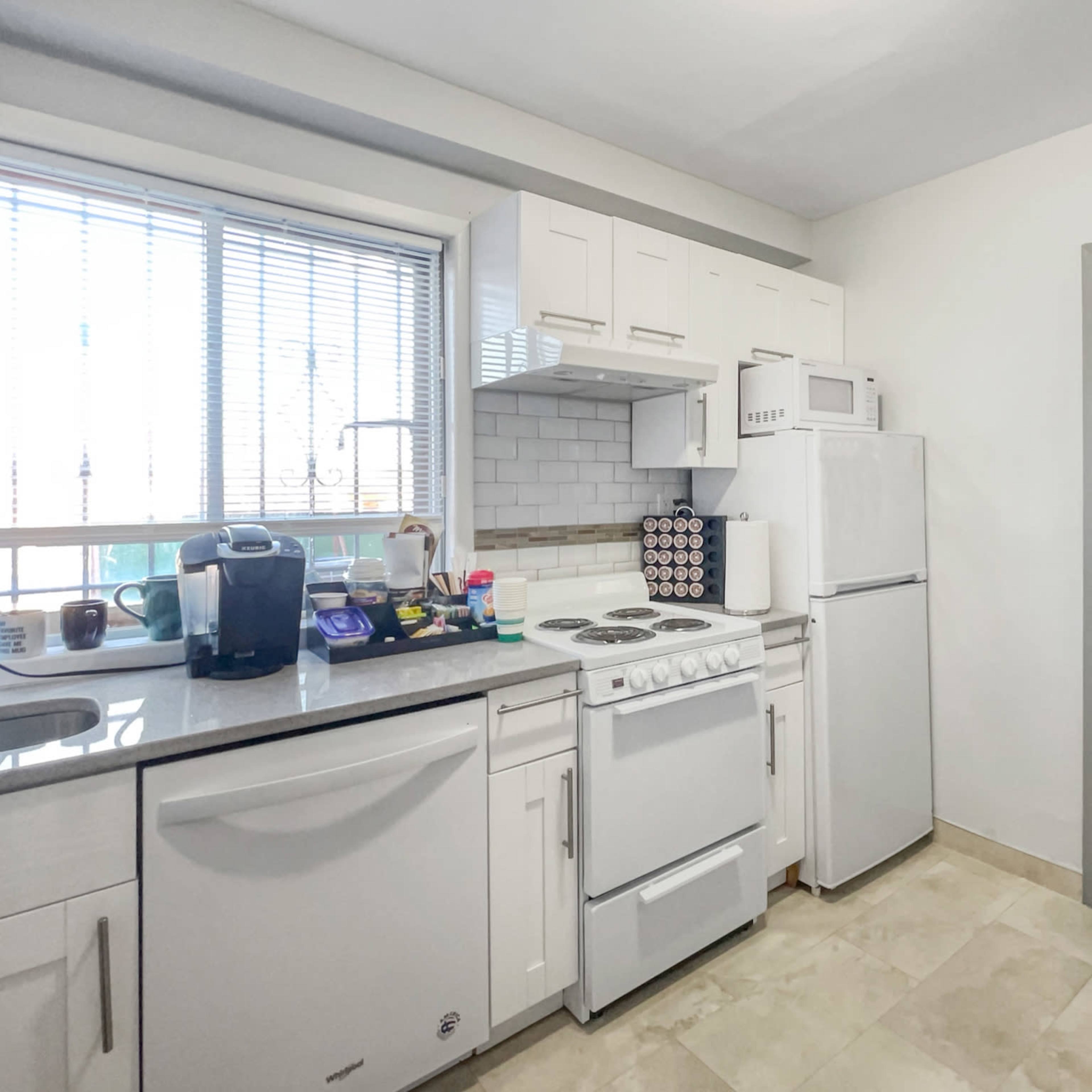 A compact kitchen with white cabinets, a stove, microwave, refrigerator, and a small dining table.