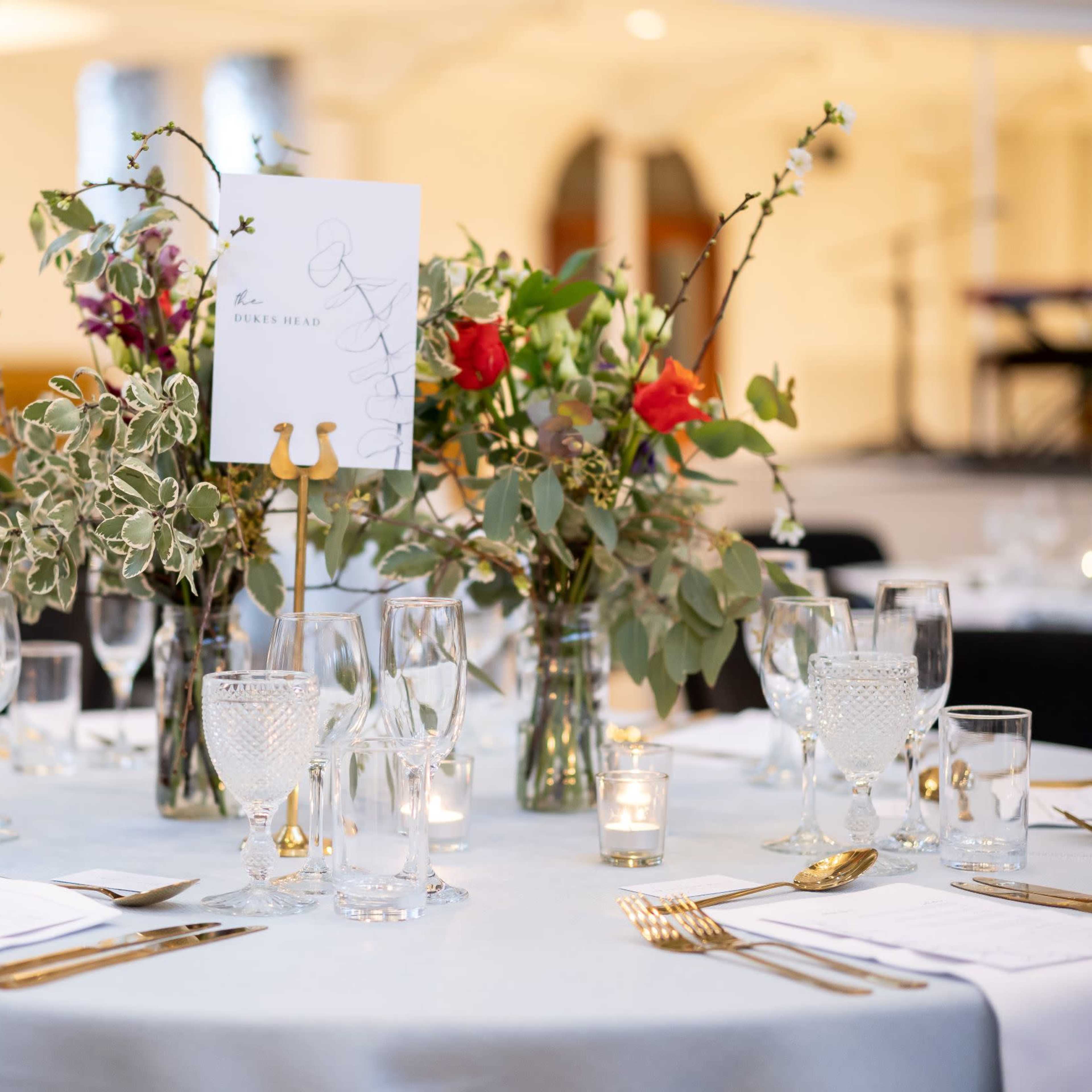Elegantly set round tables with floral centerpieces, glassware, and gold flatware in a banquet setting.