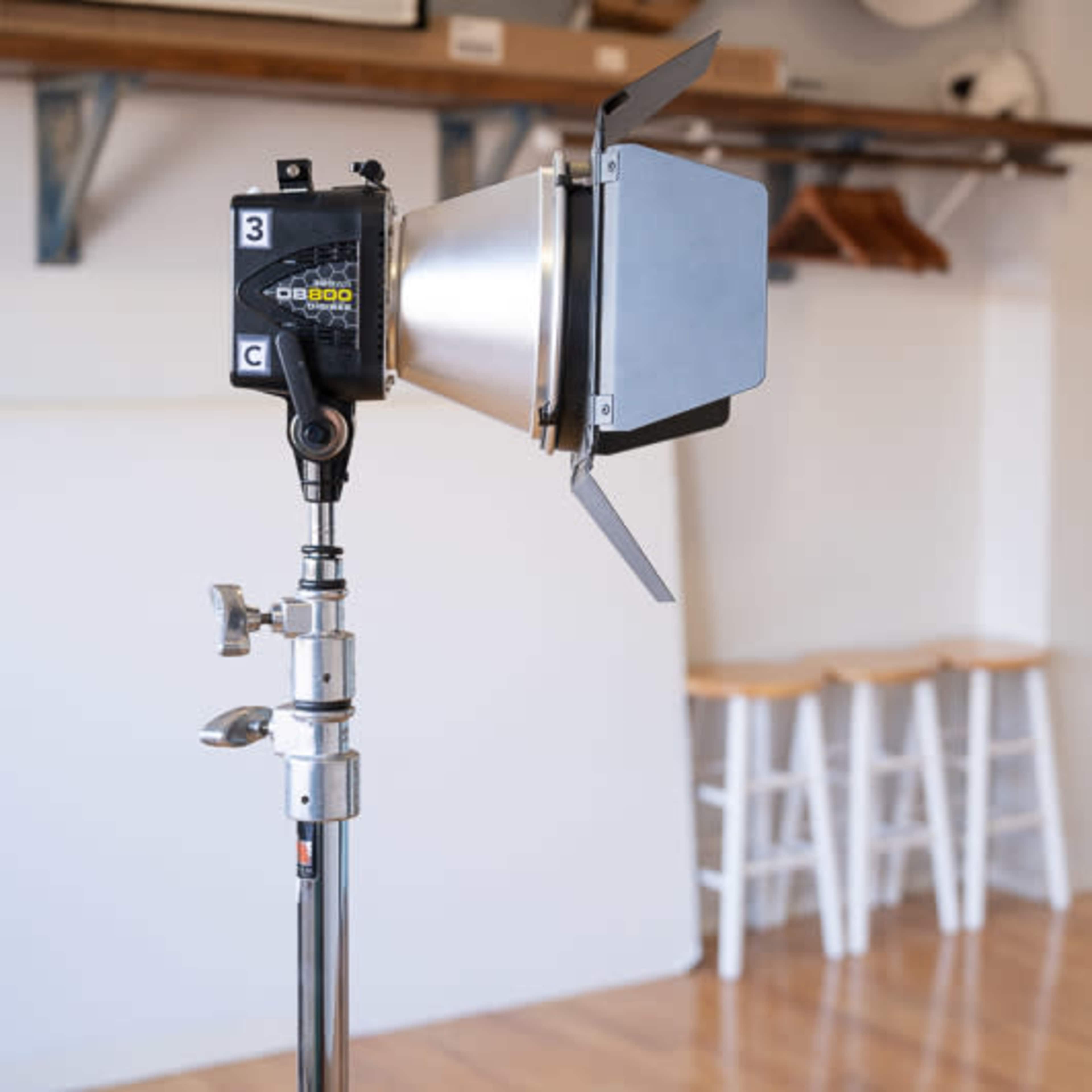 A spotlight is set up on a stand in a brightly lit room with wooden floors and a vanity area in the background.