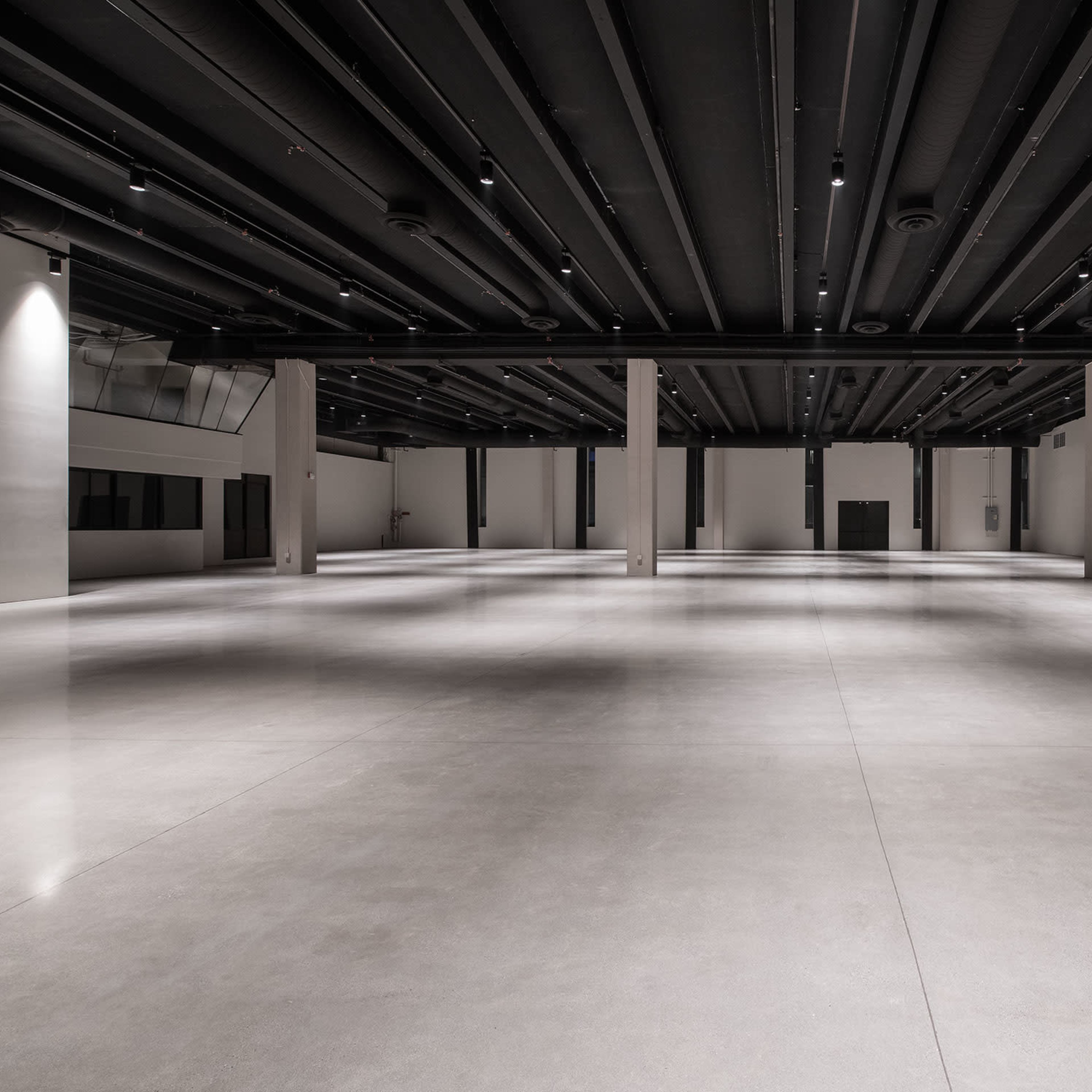 A large, empty indoor space with polished concrete flooring and exposed ceiling beams.