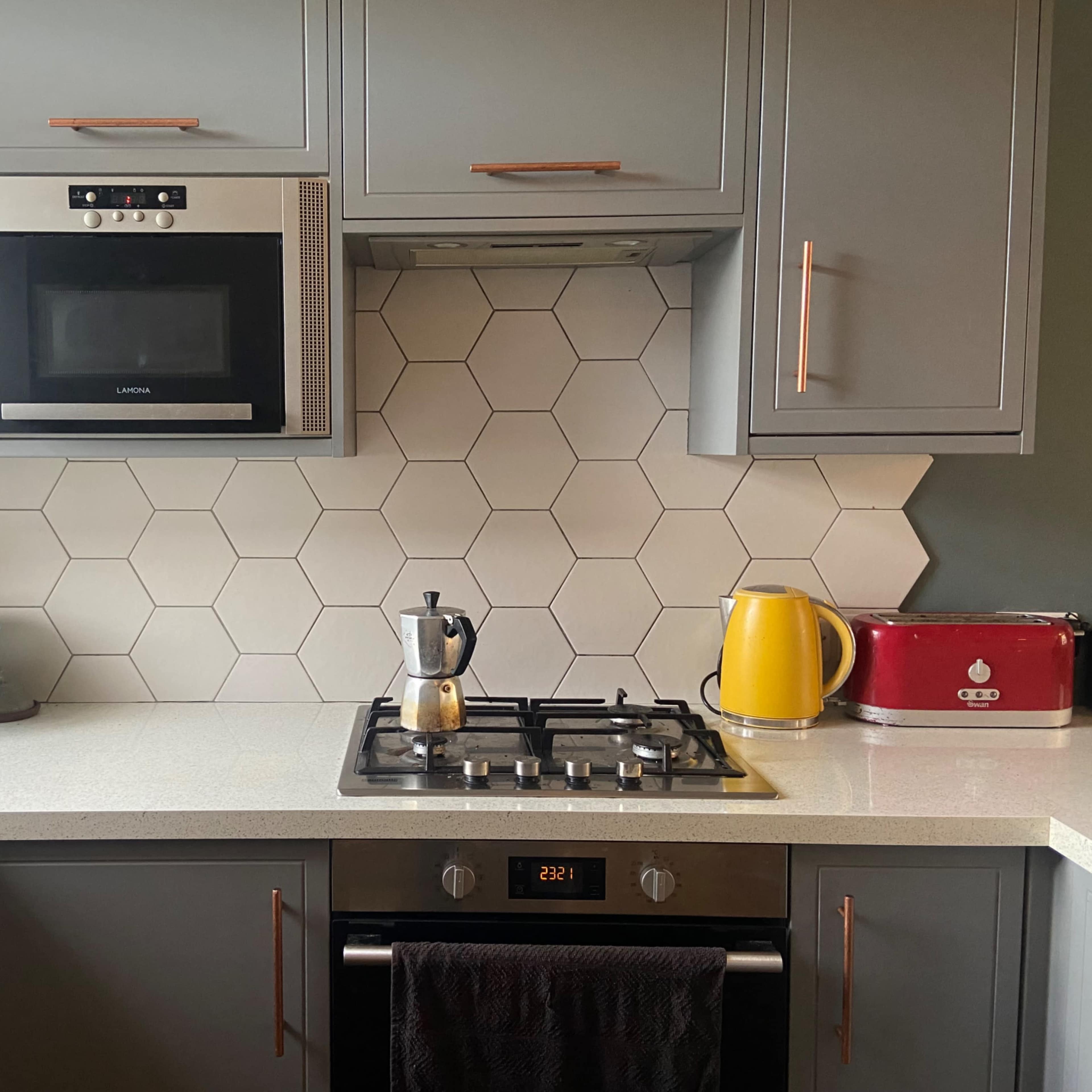 A modern kitchen features a hexagonal tile backsplash, a gas stove with a coffee maker, and various small appliances, including a kettle and a toaster.