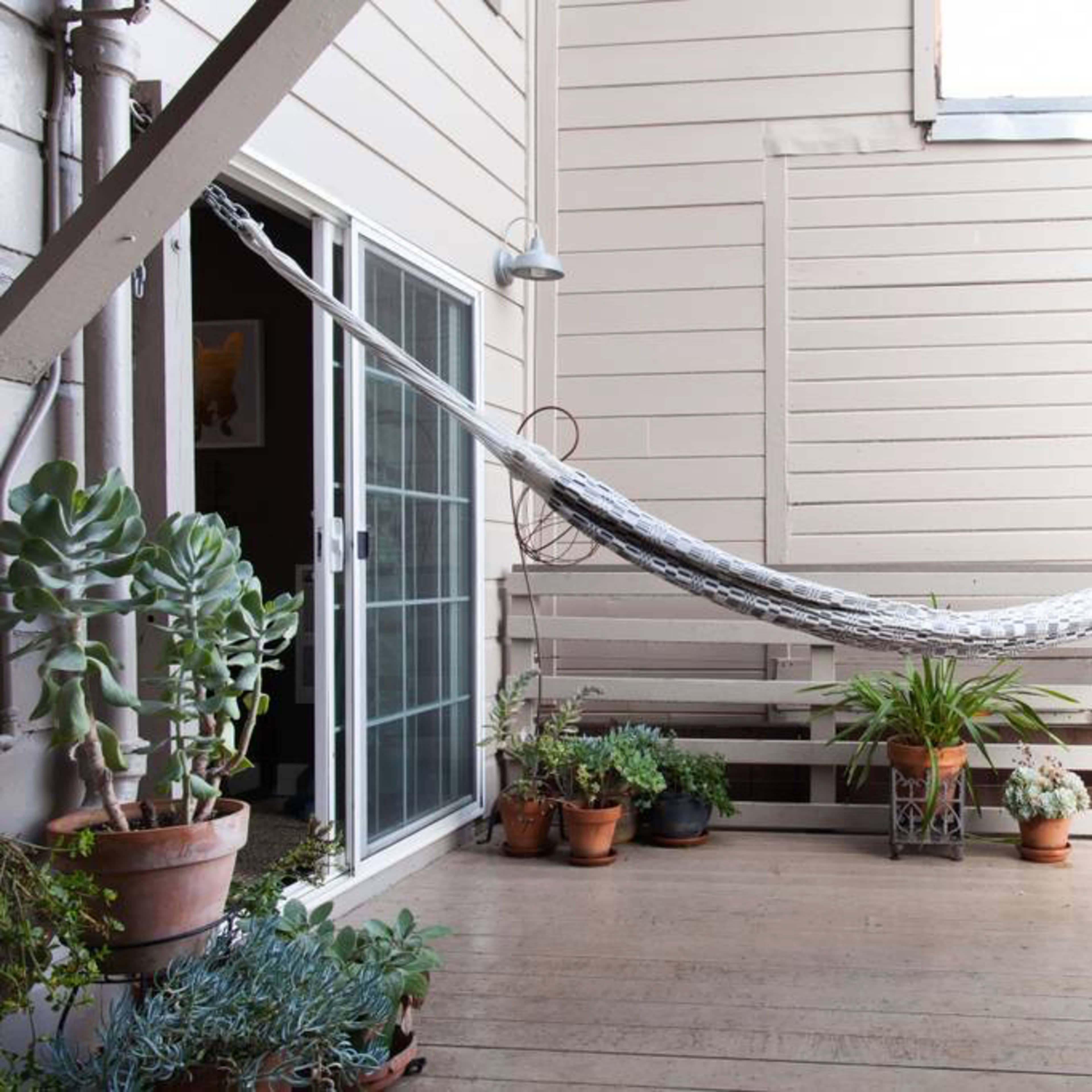 A hammock is suspended between wooden beams on a patio surrounded by potted plants.