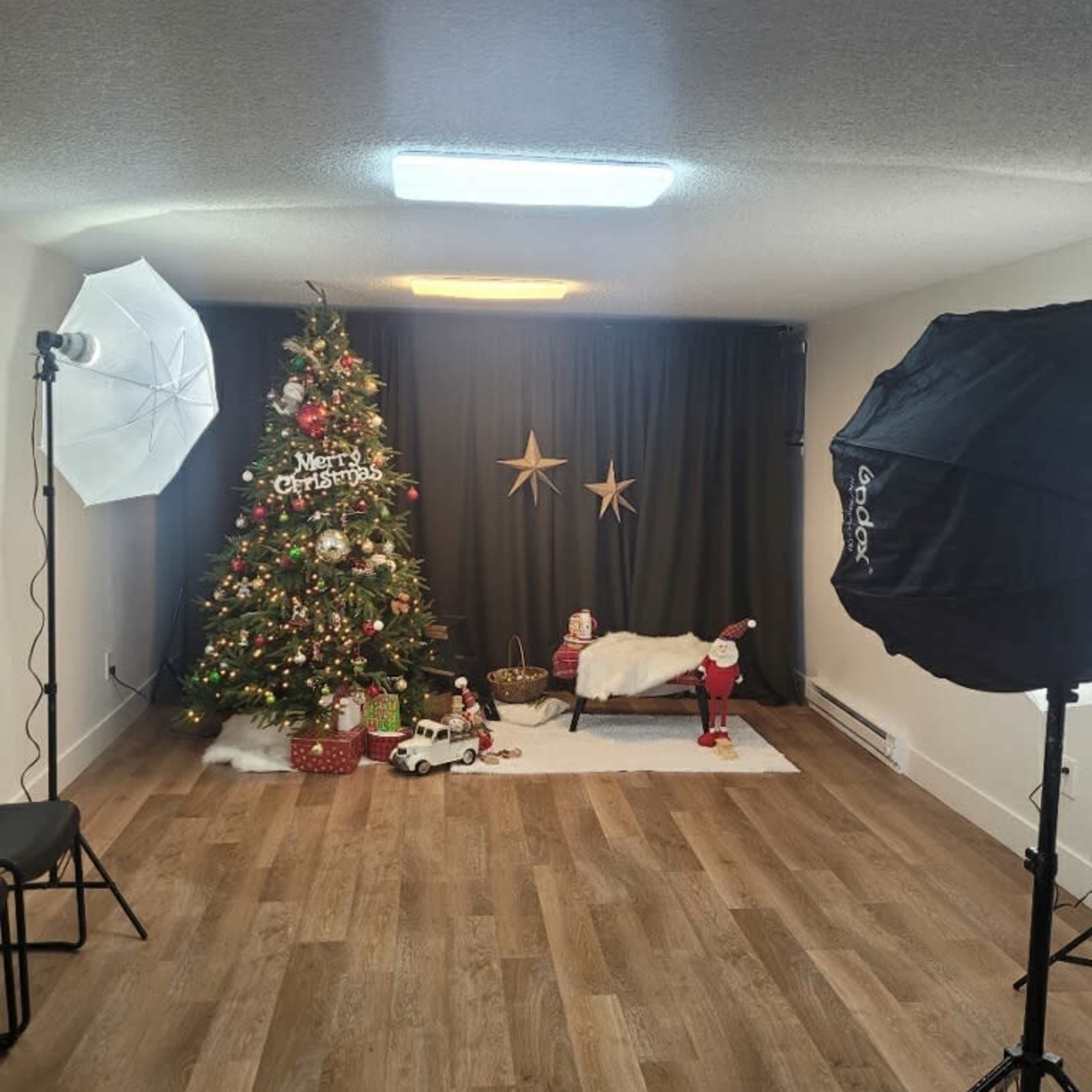A decorated Christmas set featuring a Christmas tree, a bed with a blanket, and holiday props, enhanced by studio lighting.