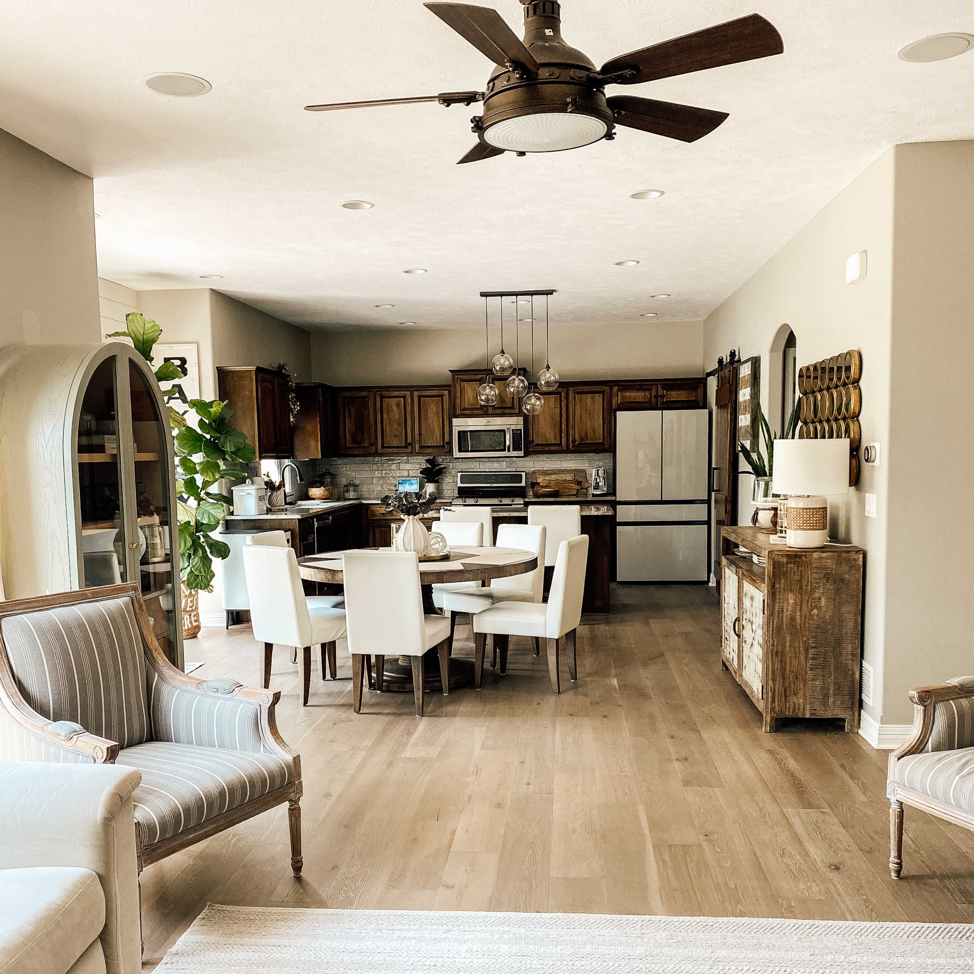 A spacious open-concept kitchen and dining area with a wooden dining table and white chairs, hardwood flooring, and a ceiling fan.
