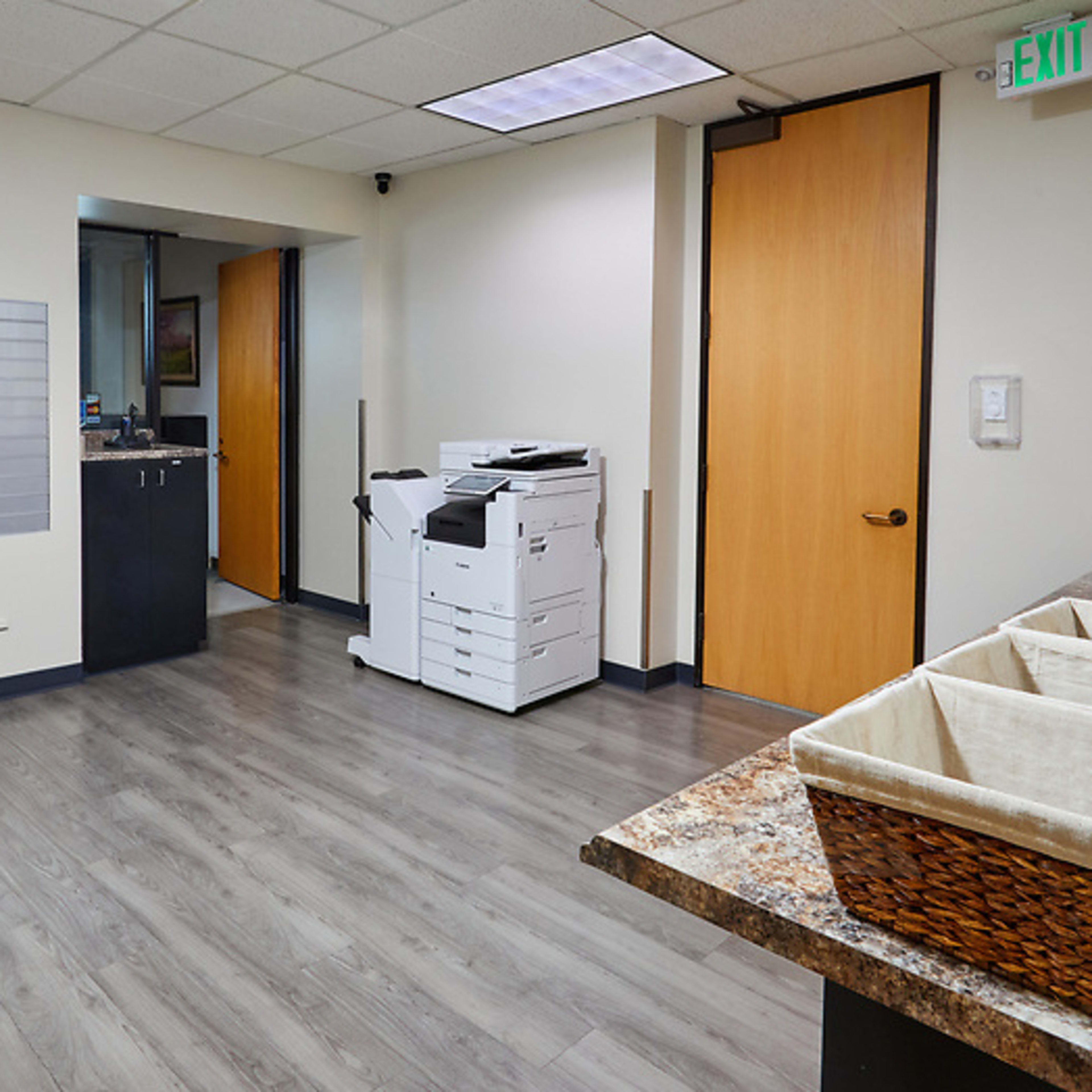 An office space featuring a row of mailboxes on the left, a printer/copier in the center, and a counter with storage baskets on the right.
