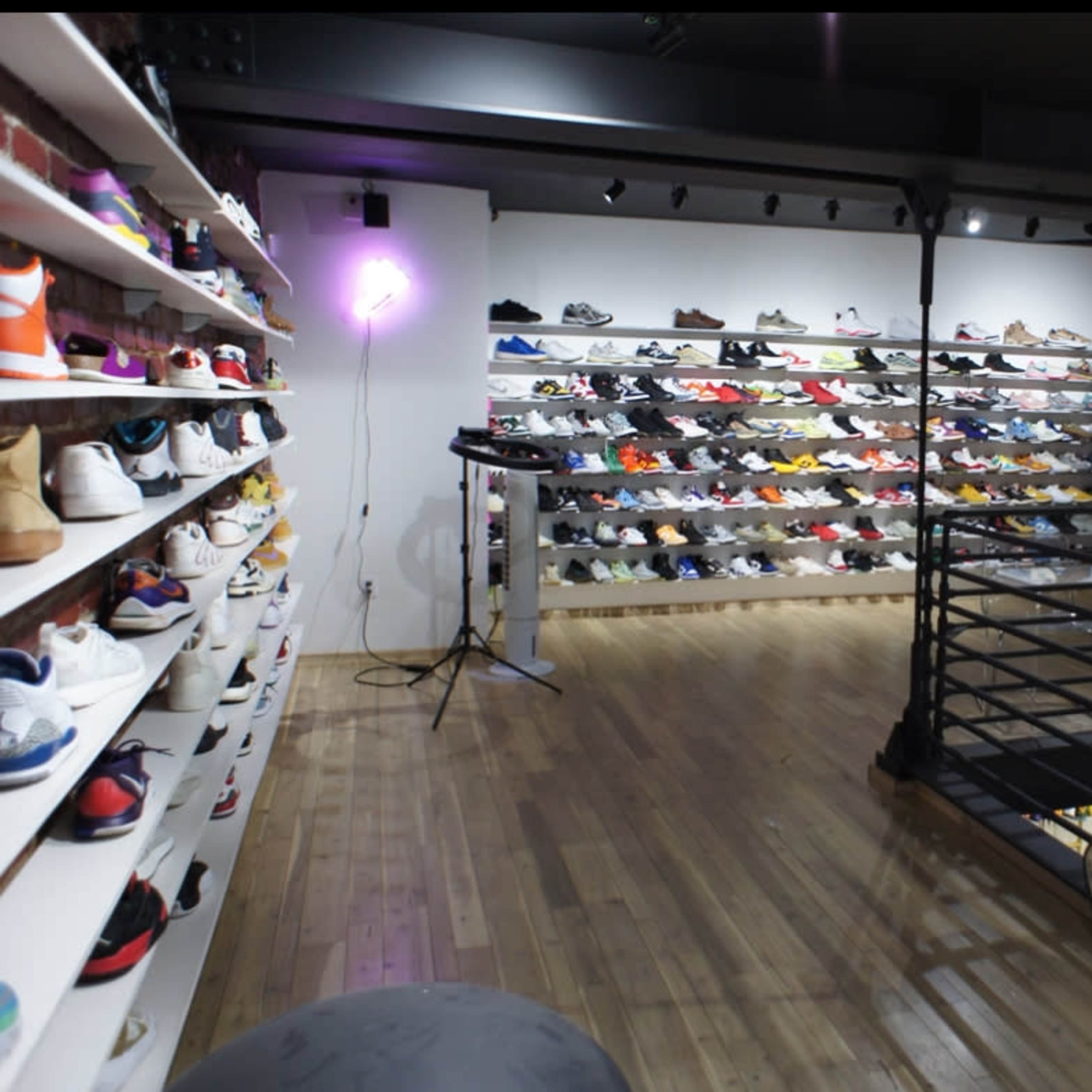 A shoe boutique displays a wide variety of sneakers on shelves against a brick wall, with a surfboard and equipment in the foreground.