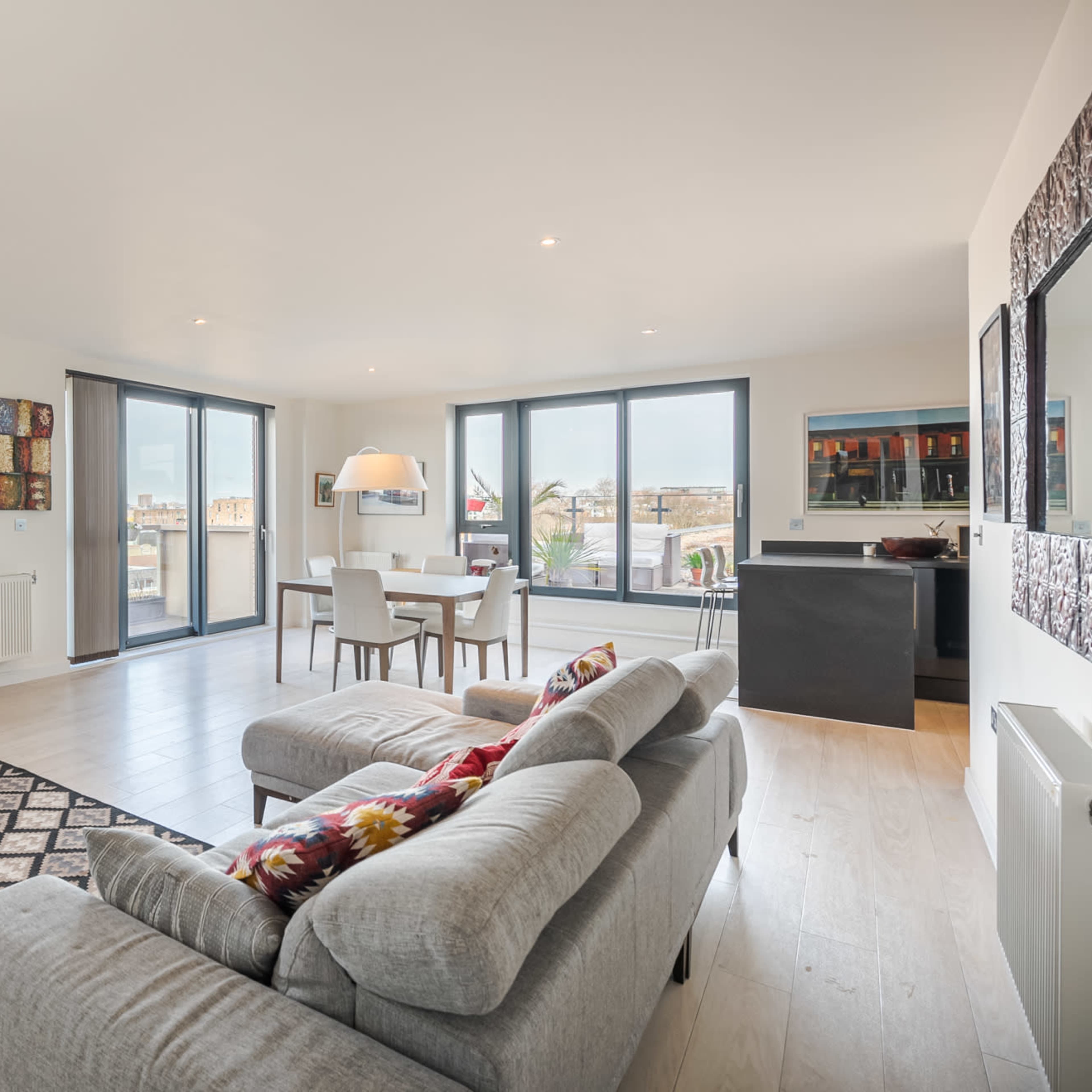 A modern, open-concept living area with a leather couch, a patterned rug, and large windows allowing natural light to fill the space.