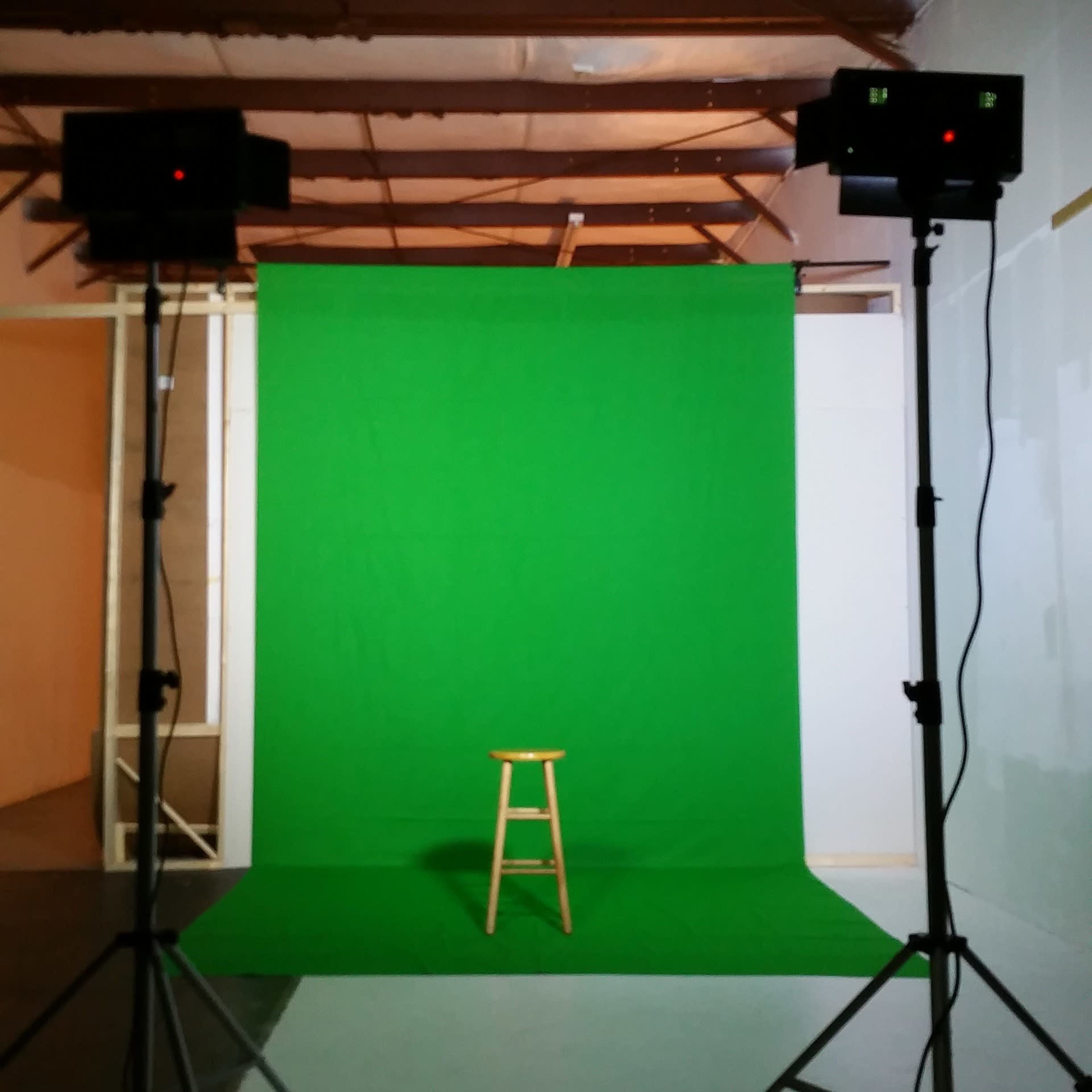 A studio setup with a green backdrop and a wooden stool positioned in front, illuminated by two lights on tripods.