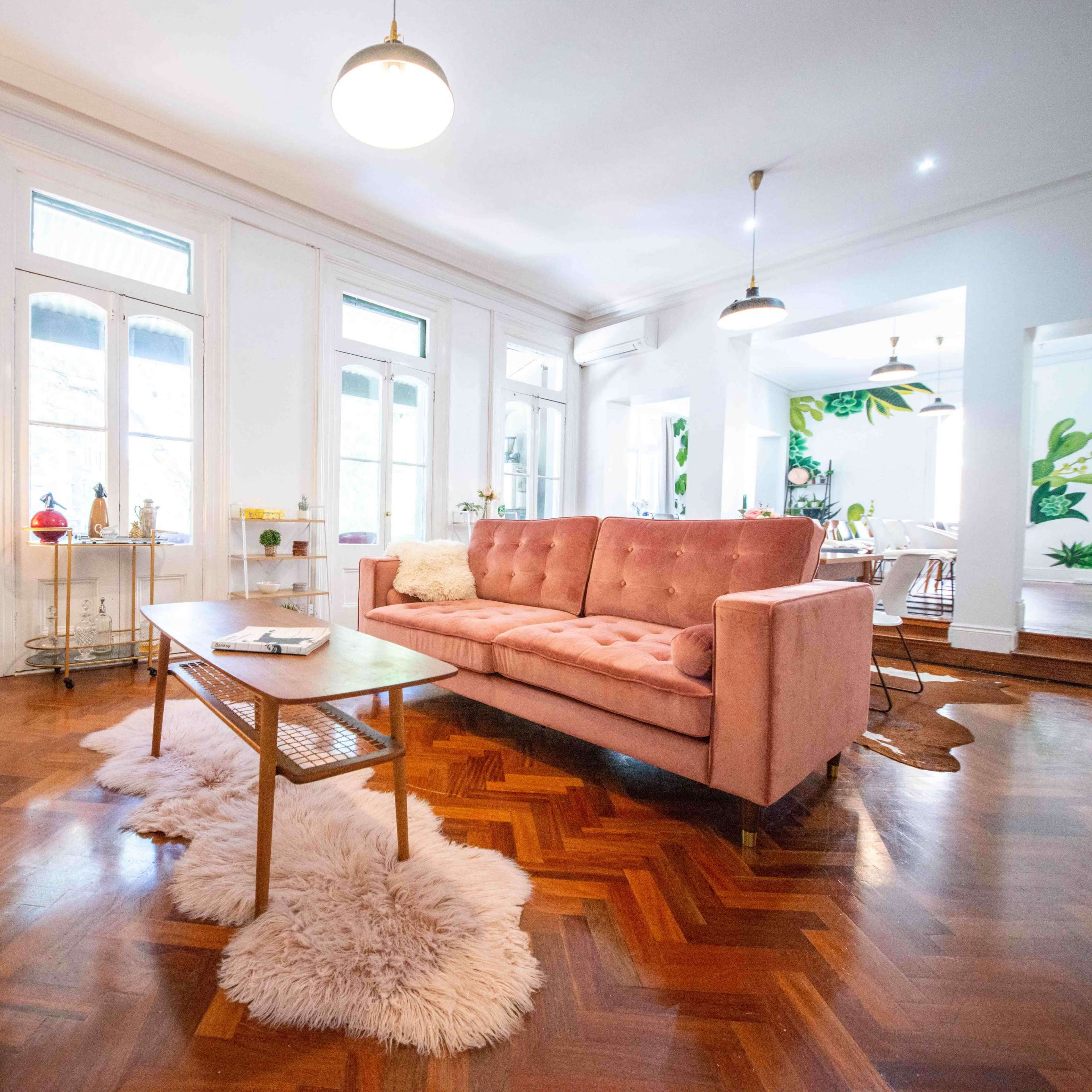 The living room features a pink sofa, a wooden coffee table, and a decorative fur rug, with large windows allowing natural light to fill the space.