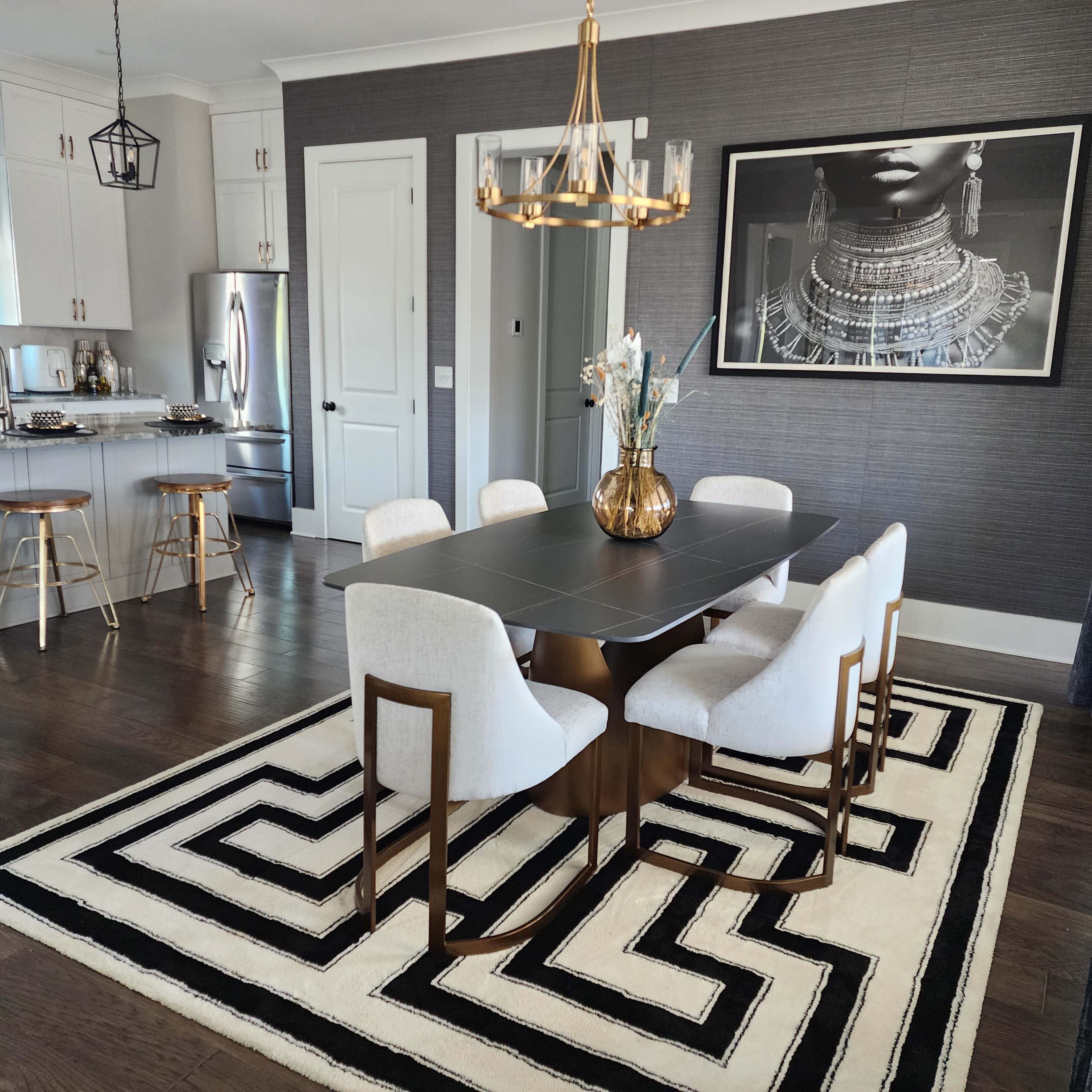 A modern dining area with a rectangular table surrounded by six chairs, a geometric rug, and a decorative chandelier overhead.
