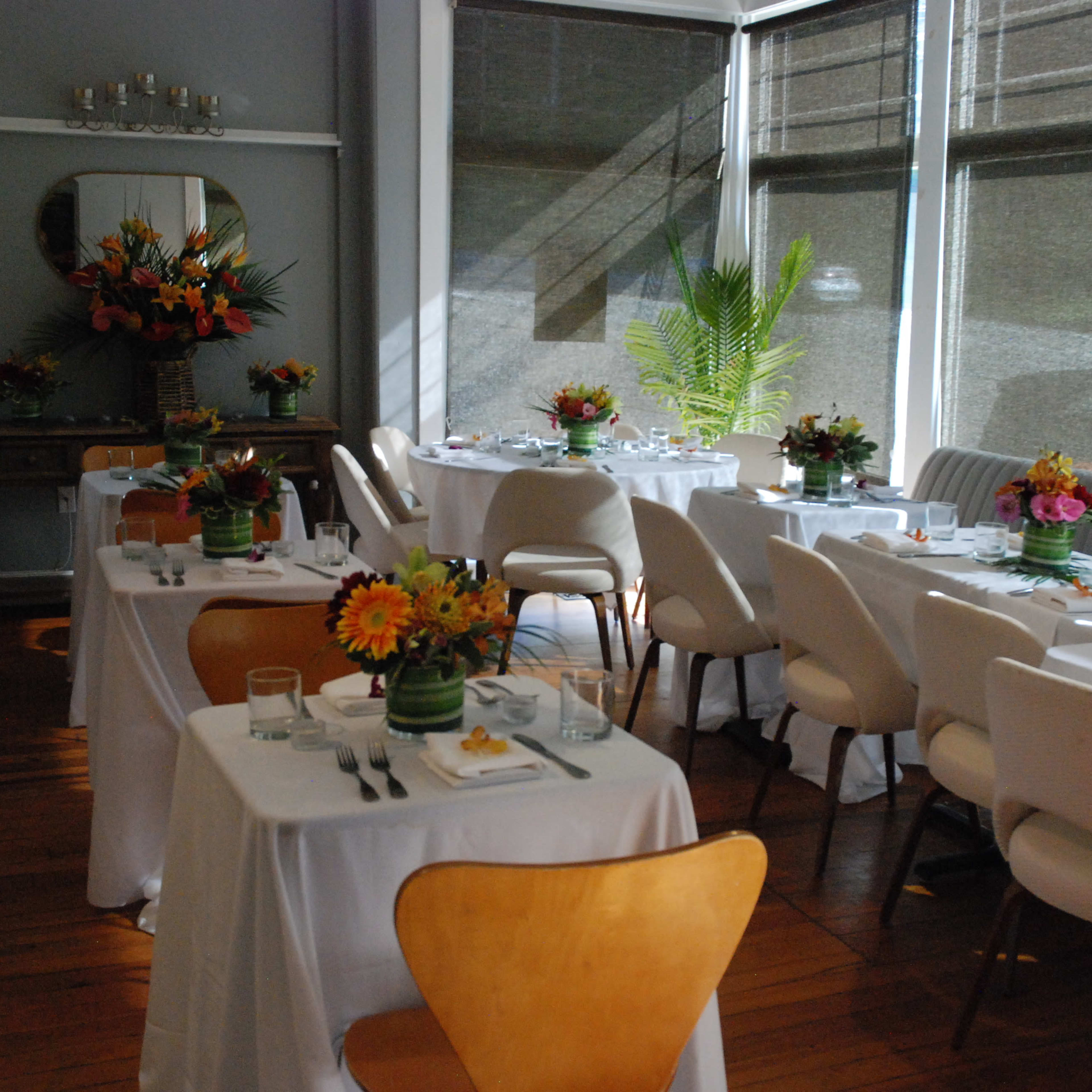 A bright, airy dining area with several tables set for a meal, each adorned with floral centerpieces.