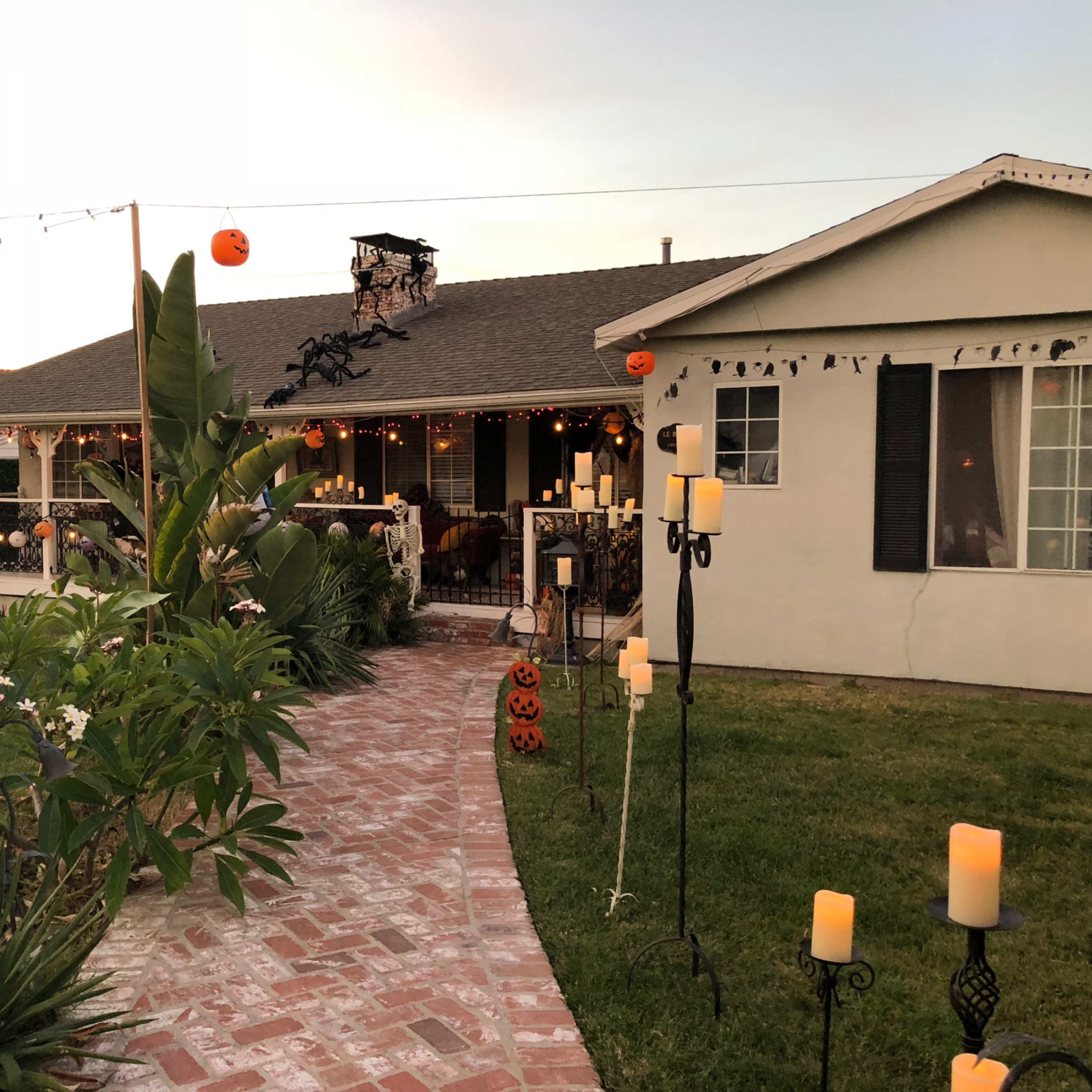 A pathway leads to a decorated house with Halloween-themed candles and pumpkins in the yard.