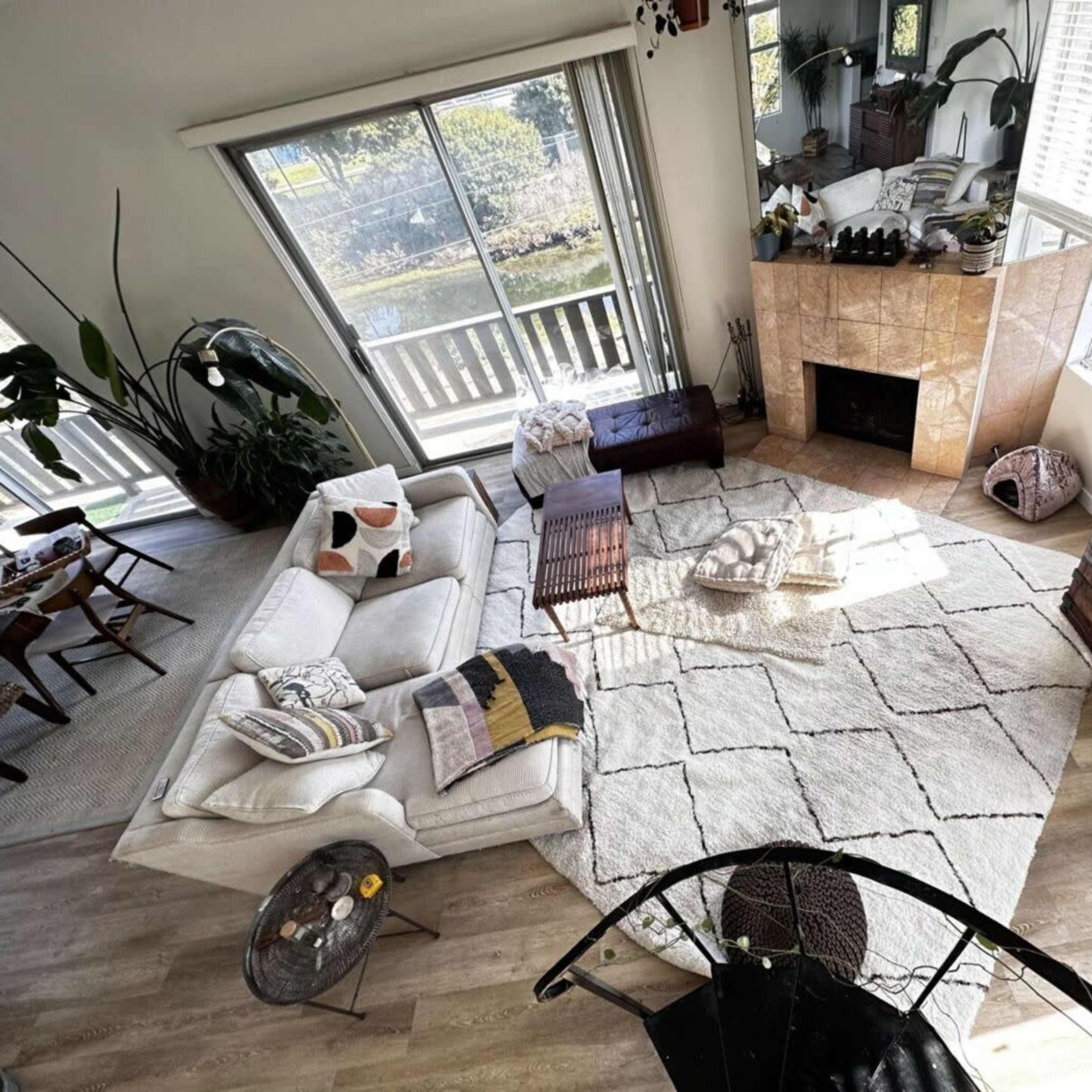 A spacious living room with a large sectional sofa, a coffee table, and a fireplace, illuminated by natural light from windows overlooking a garden.