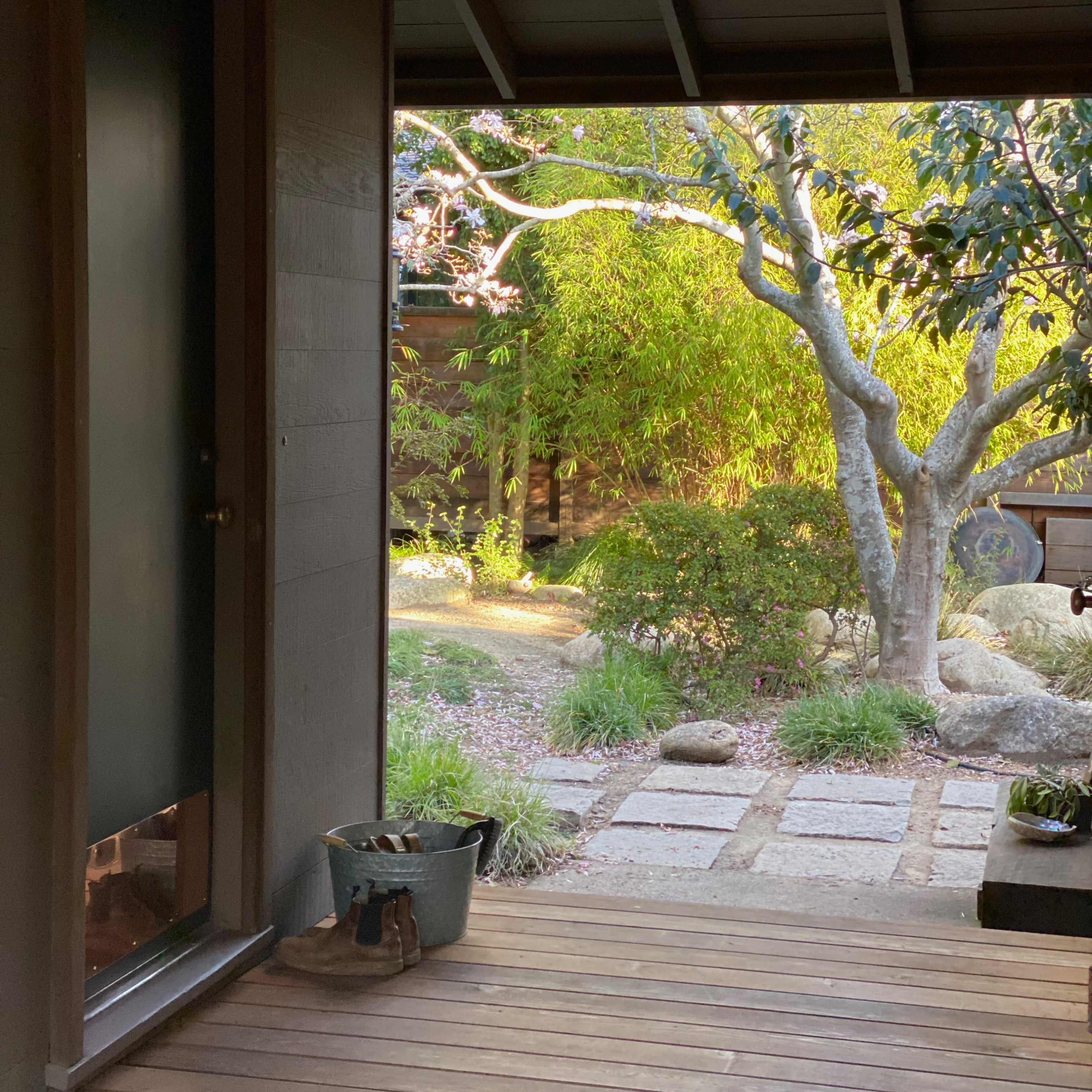 A doorway leads to a garden featuring pathways, stone walkways, and a variety of plants.