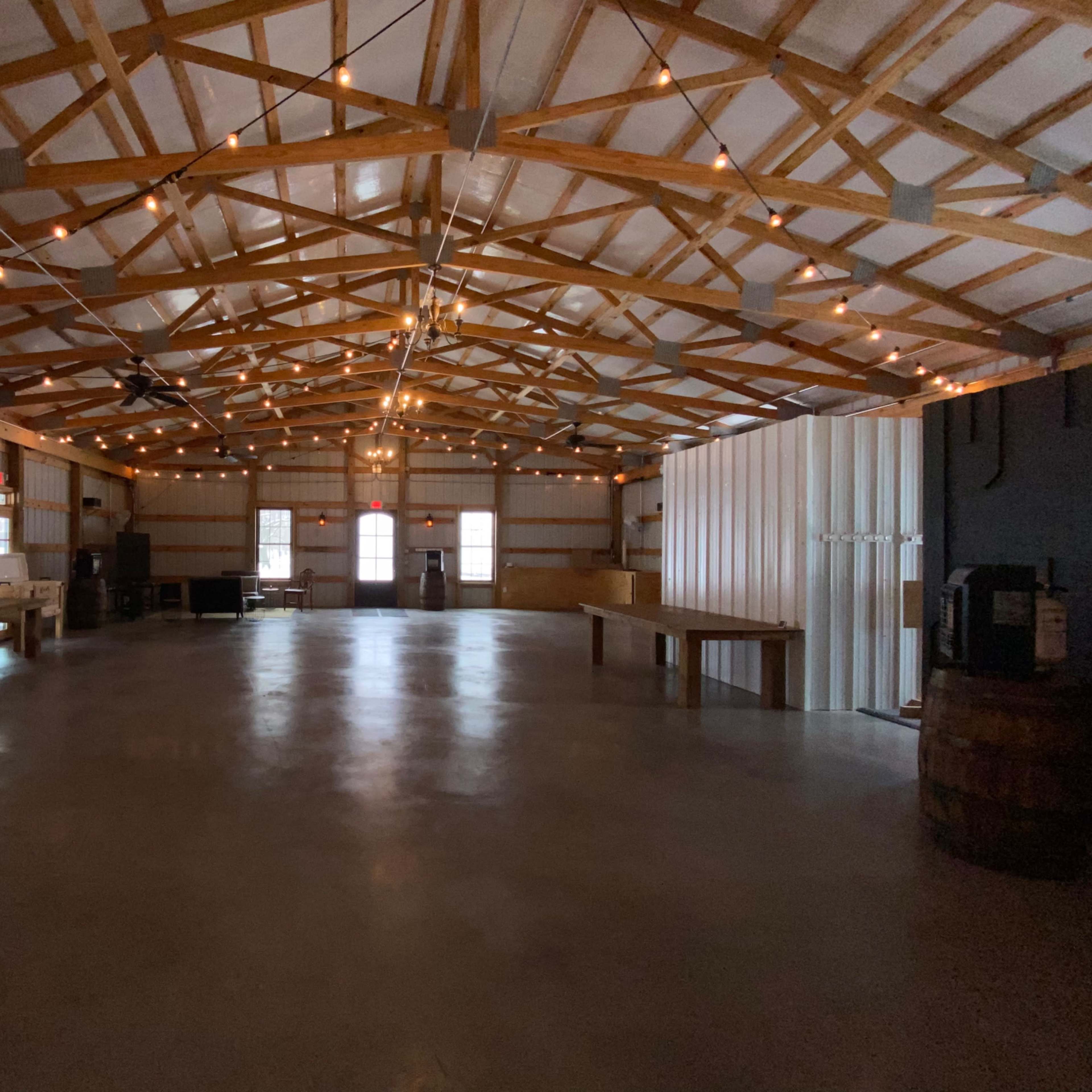 An empty indoor venue with wooden beams, string lights overhead, and a polished concrete floor.
