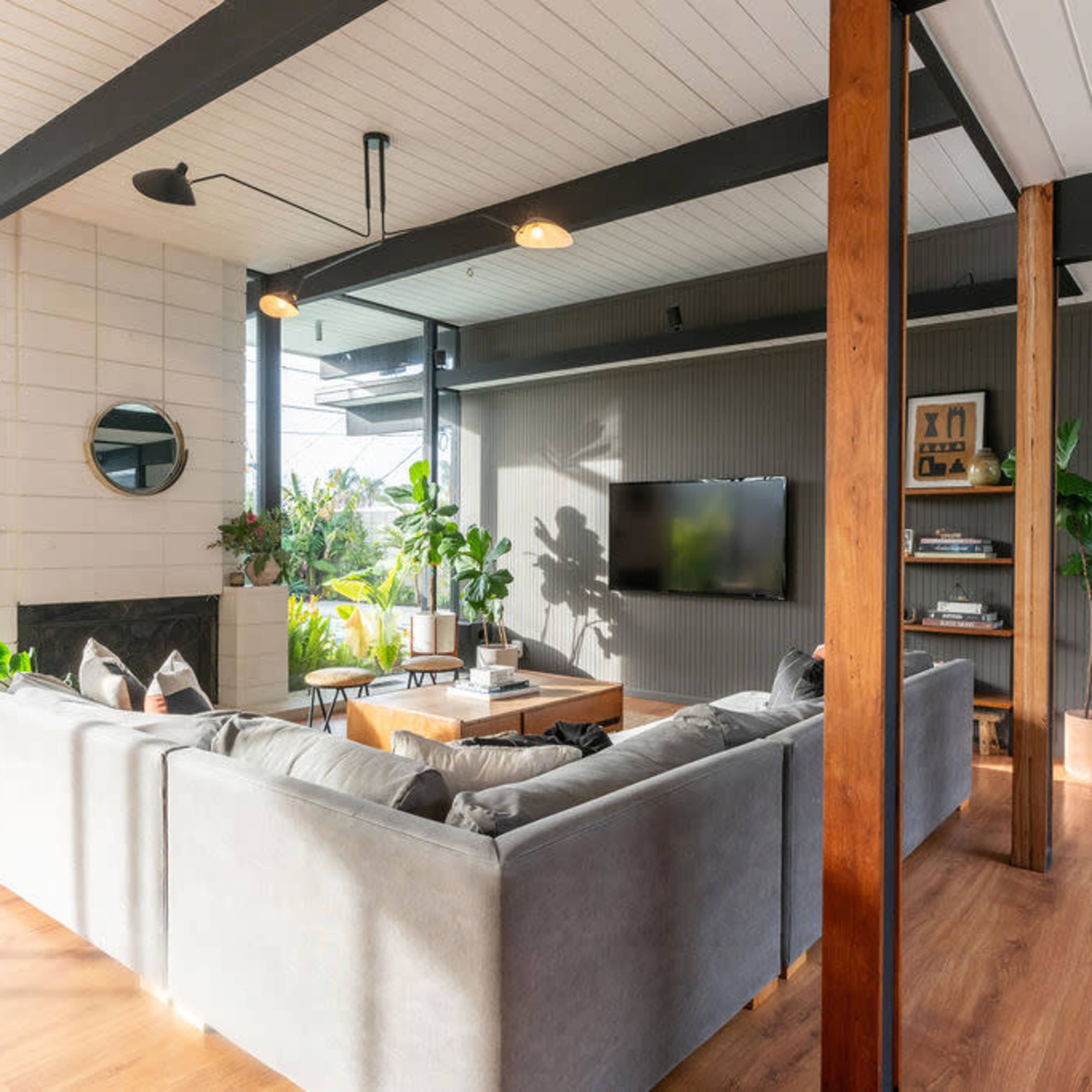 A modern living room featuring a large gray sectional sofa, wooden accents, potted plants, and a television mounted on the wall.