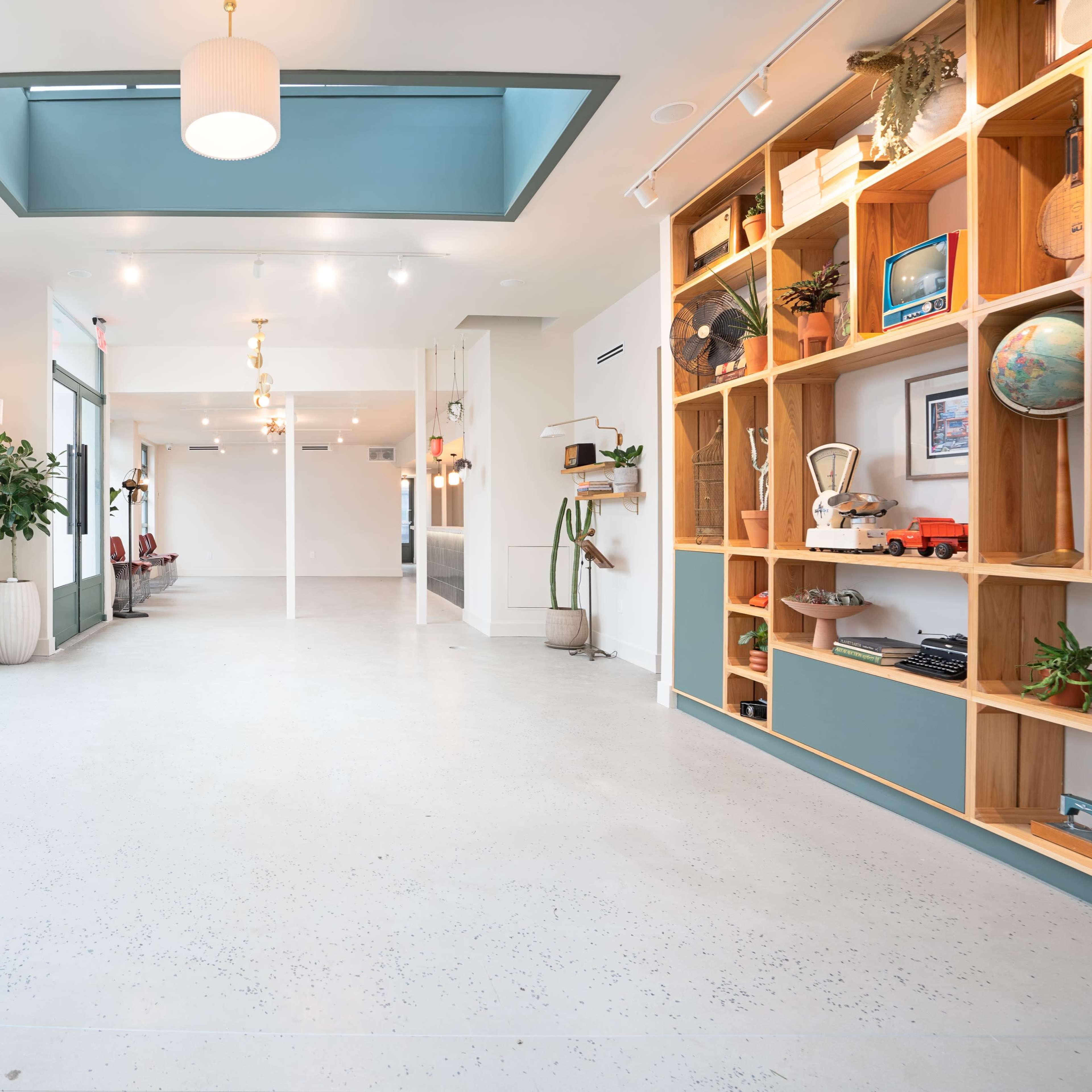 A bright, spacious interior with large windows, a light-colored floor, and a wooden shelving unit displaying various decorative items.
