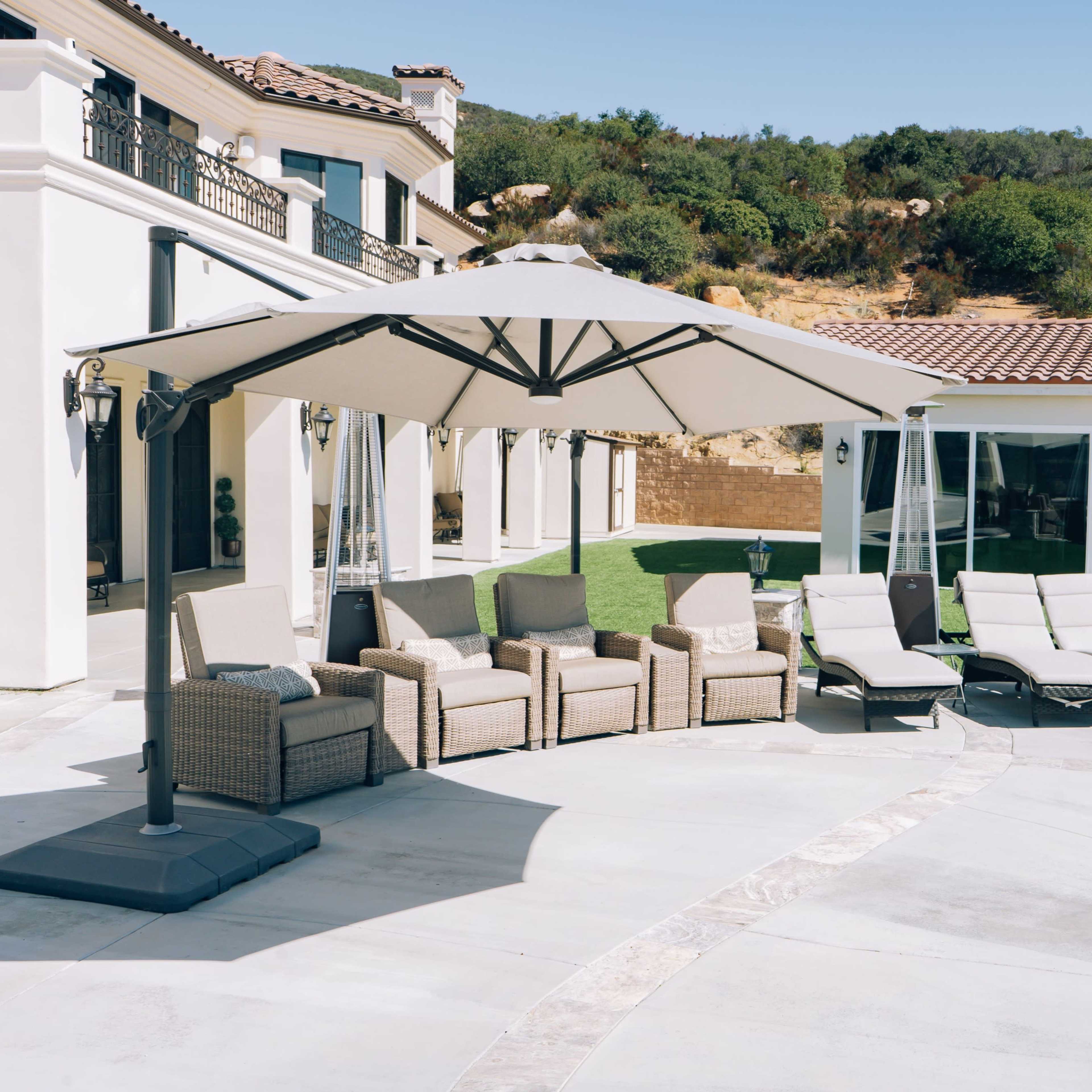 A spacious outdoor area features a set of wicker chairs and a large umbrella near a swimming pool and lounge chairs.