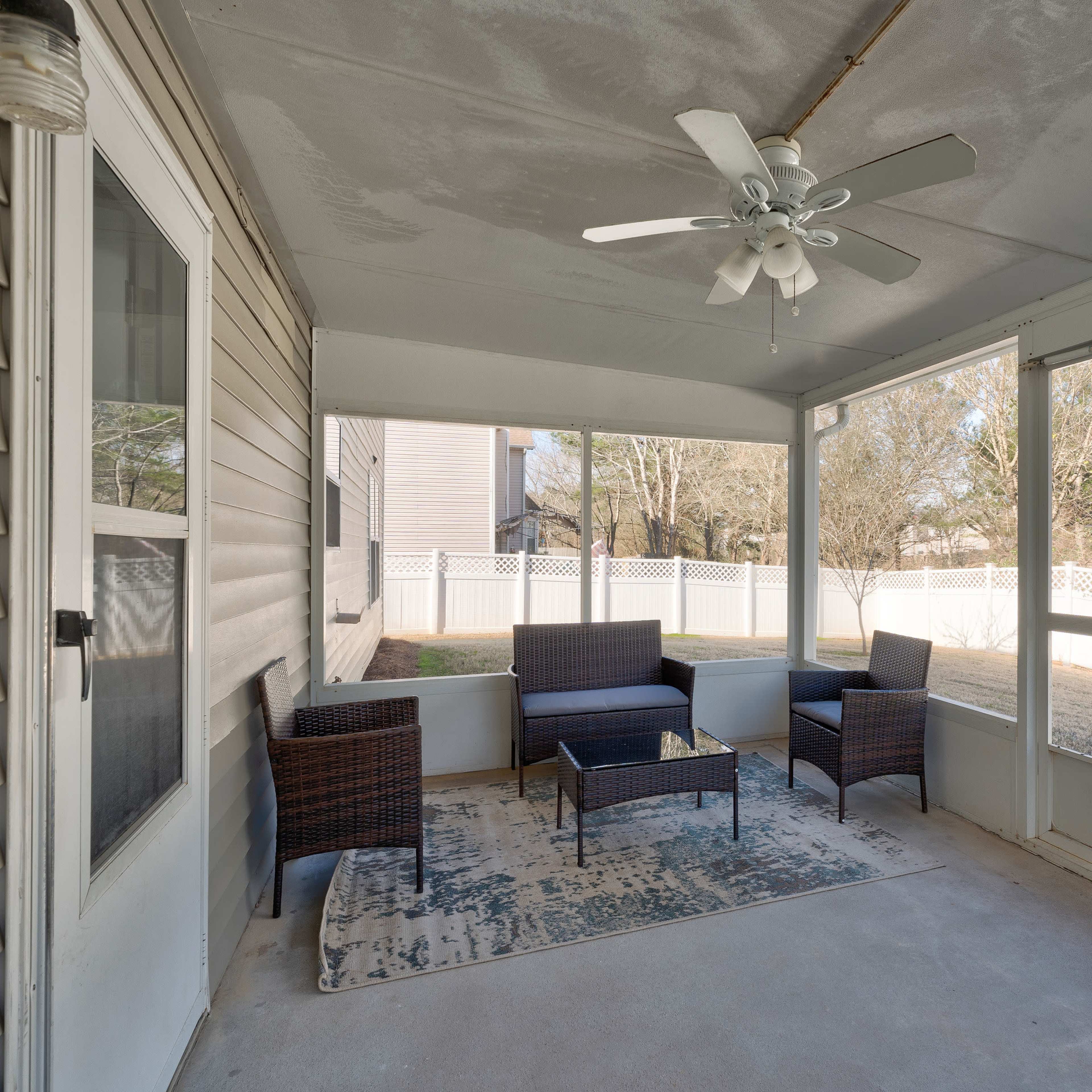 A screened-in porch featuring a ceiling fan, a seating area with wicker furniture, and a view of a backyard with a white fence.