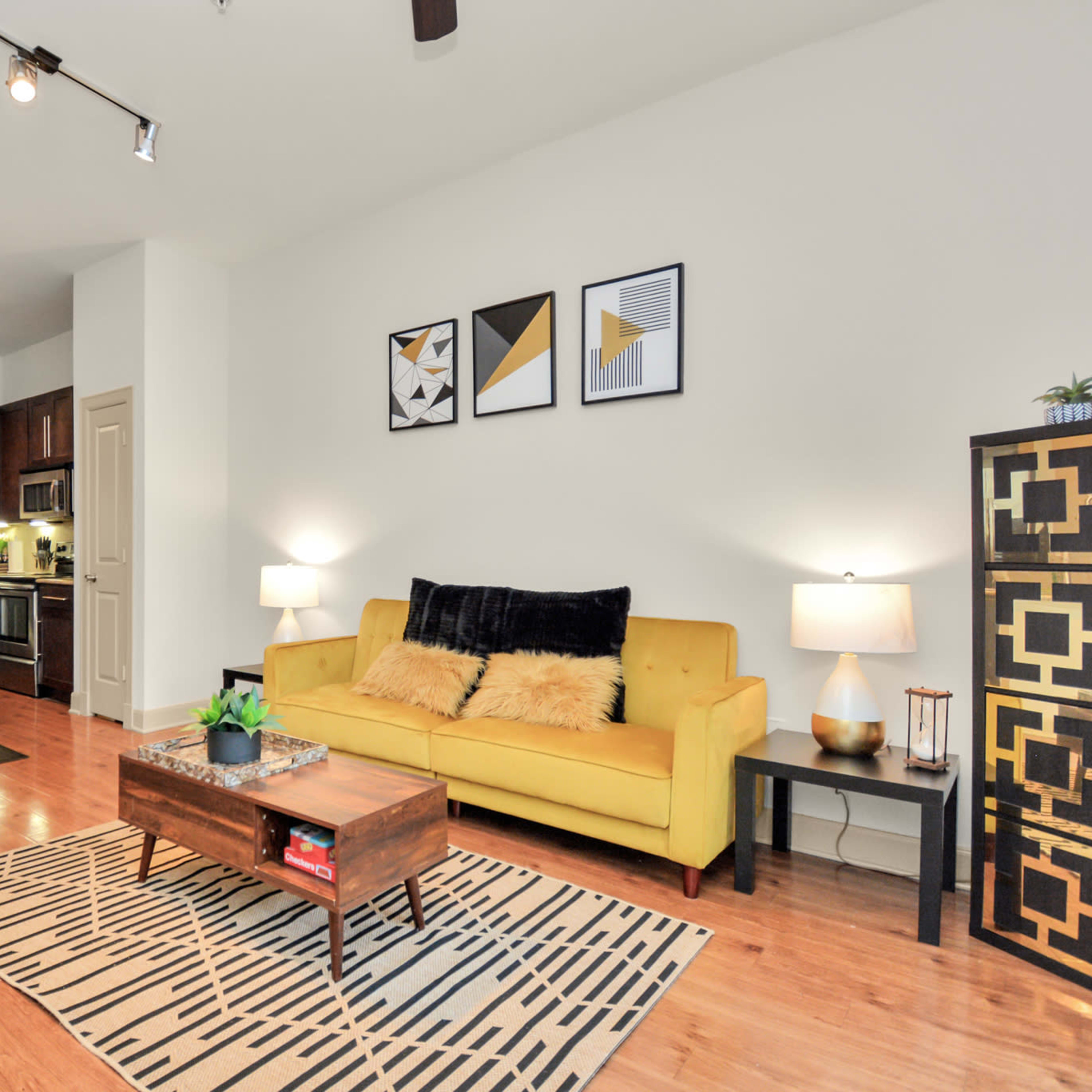 A modern living room with a yellow sofa, a coffee table on a patterned rug, and an open kitchen area in the background.