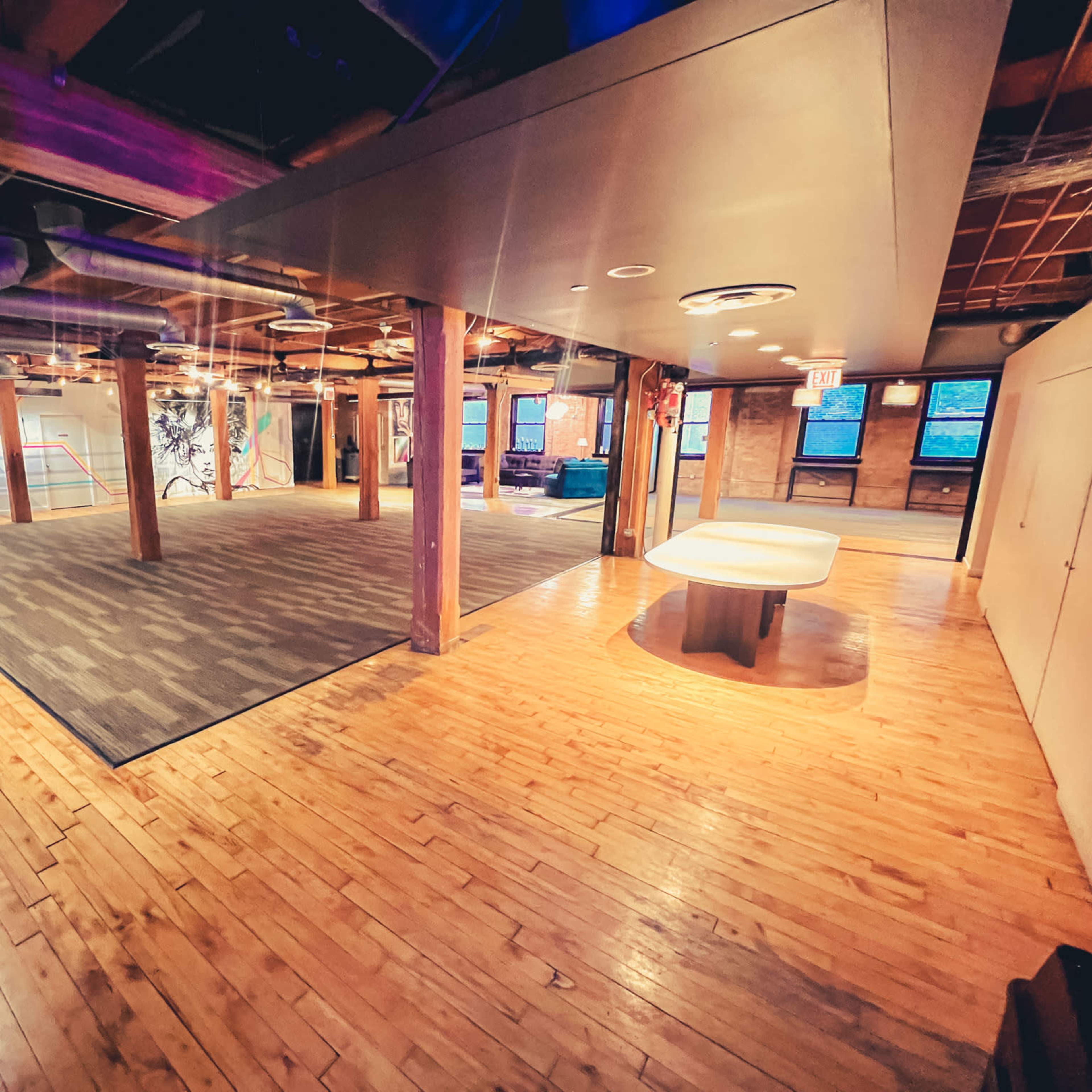 A spacious interior of a building featuring wooden floors, exposed beams, and areas with different flooring textures.