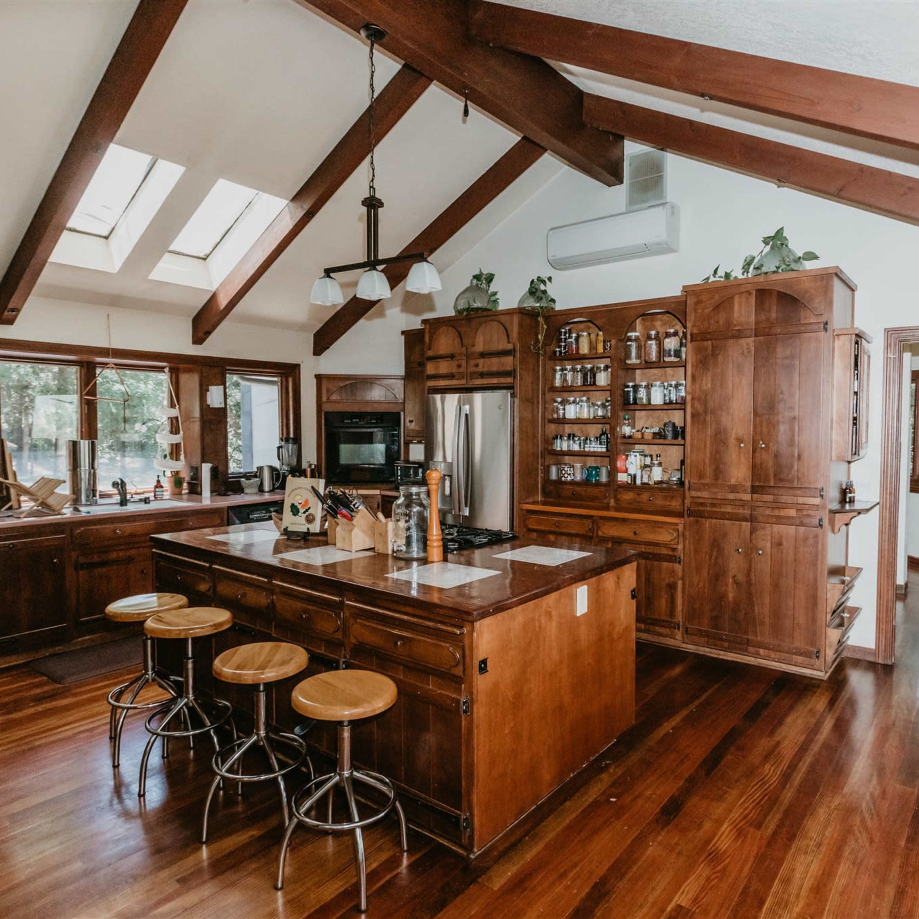 The kitchen features wooden cabinetry, a central island with seating, and skylights that illuminate the space.