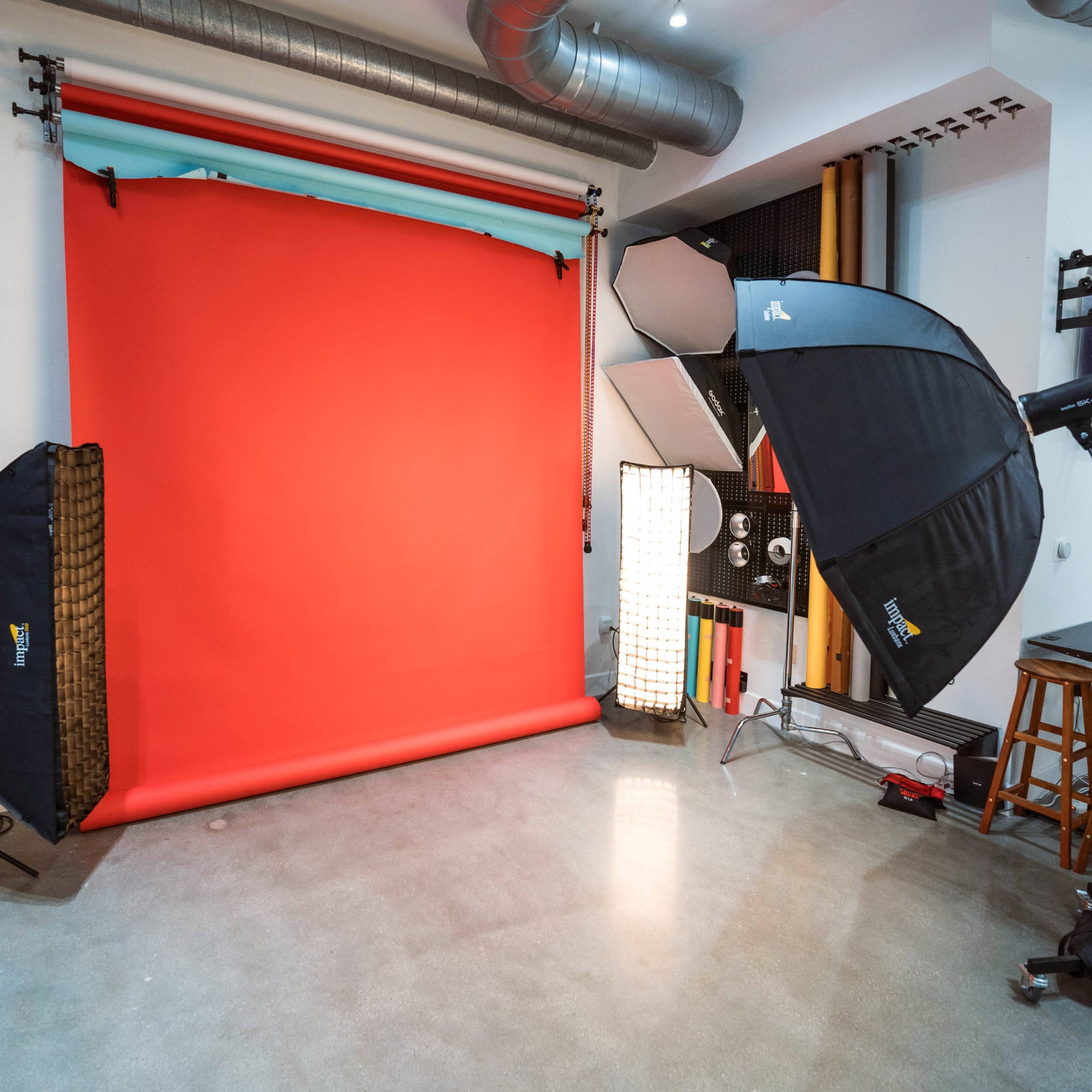 A photography studio setup with a red backdrop, lighting equipment, a ladder, and various props arranged in the space.