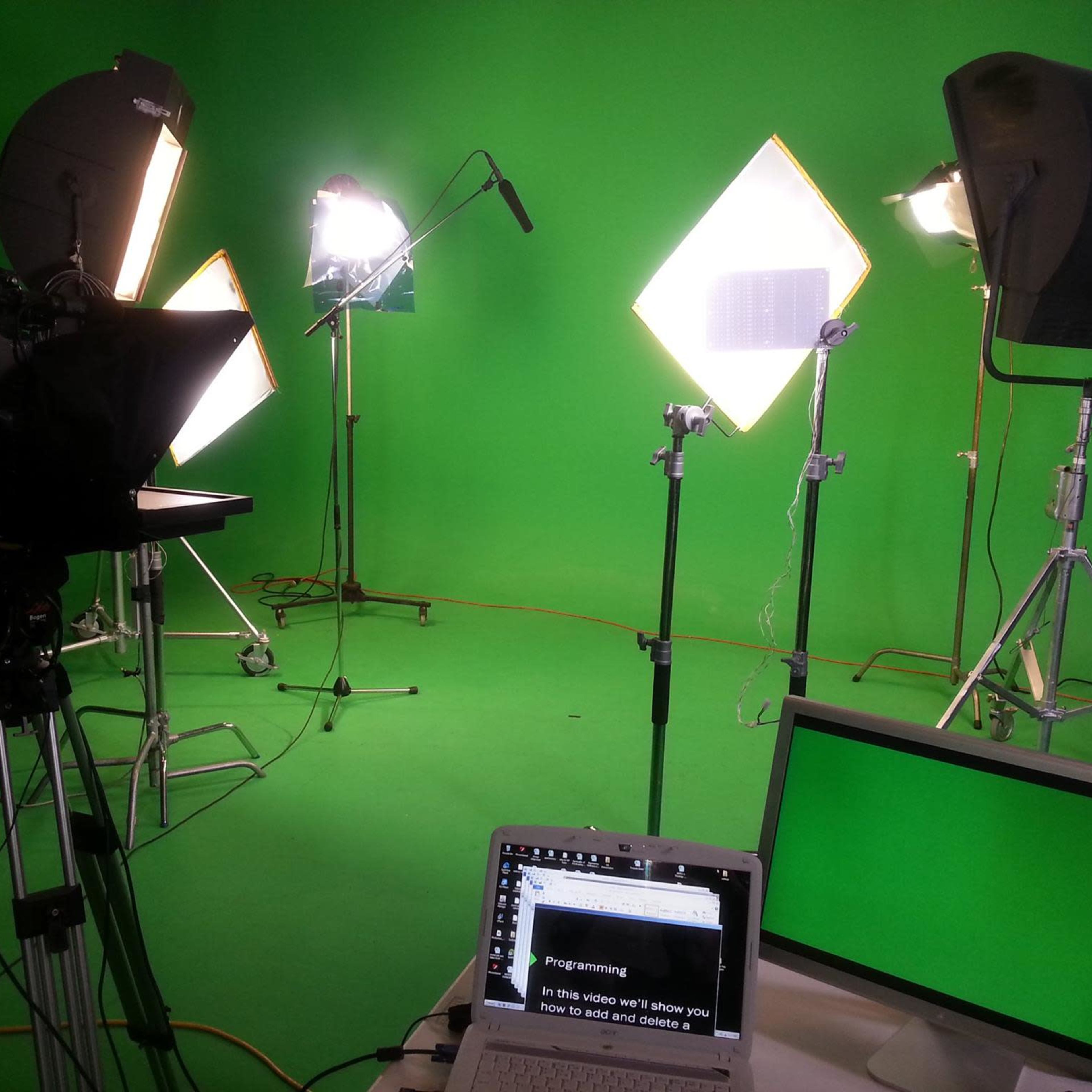 A green screen studio setup with multiple lights, a camera on a tripod, and a laptop displaying text.
