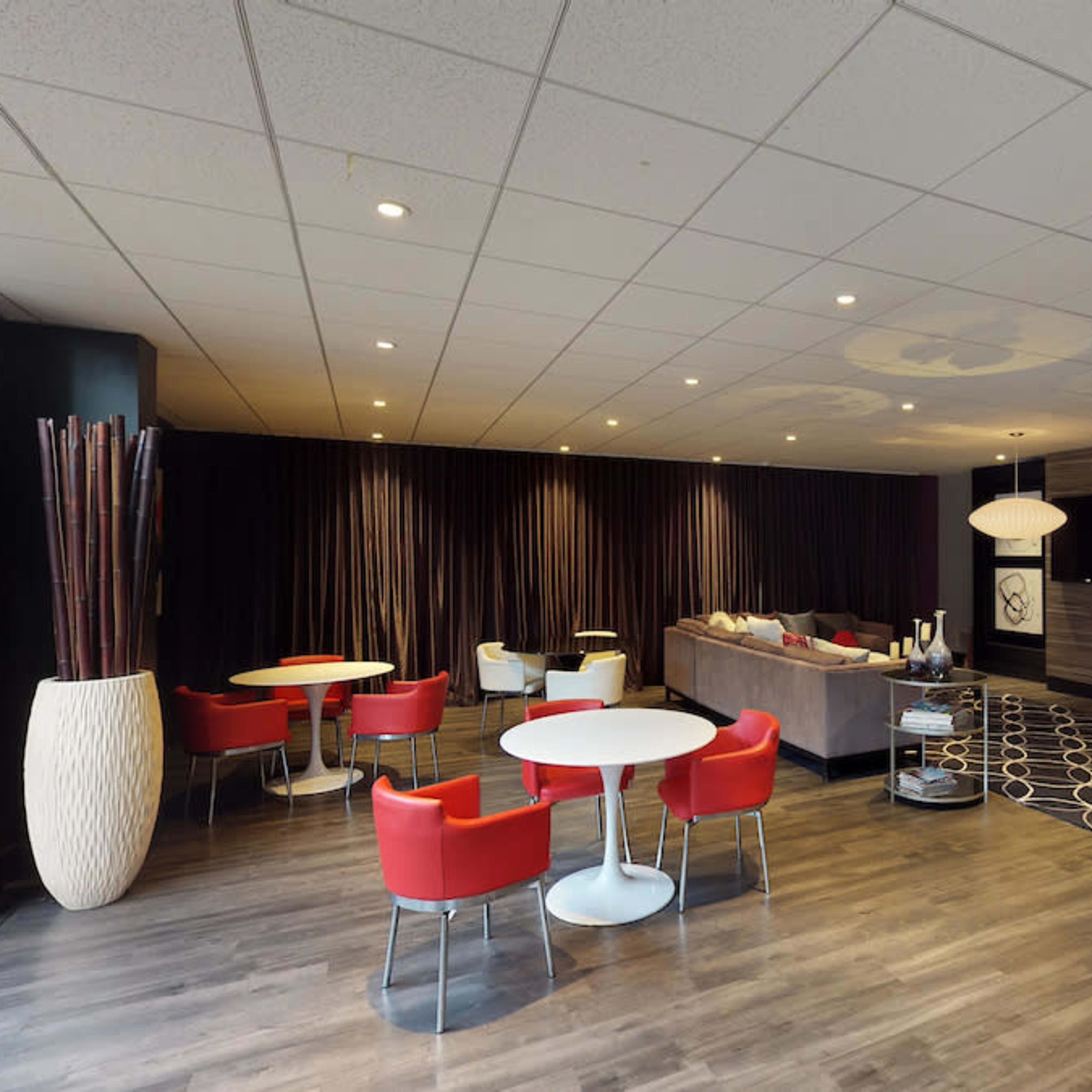 A modern lounge area with red chairs, white tables, a gray sofa, and decorative wall art.