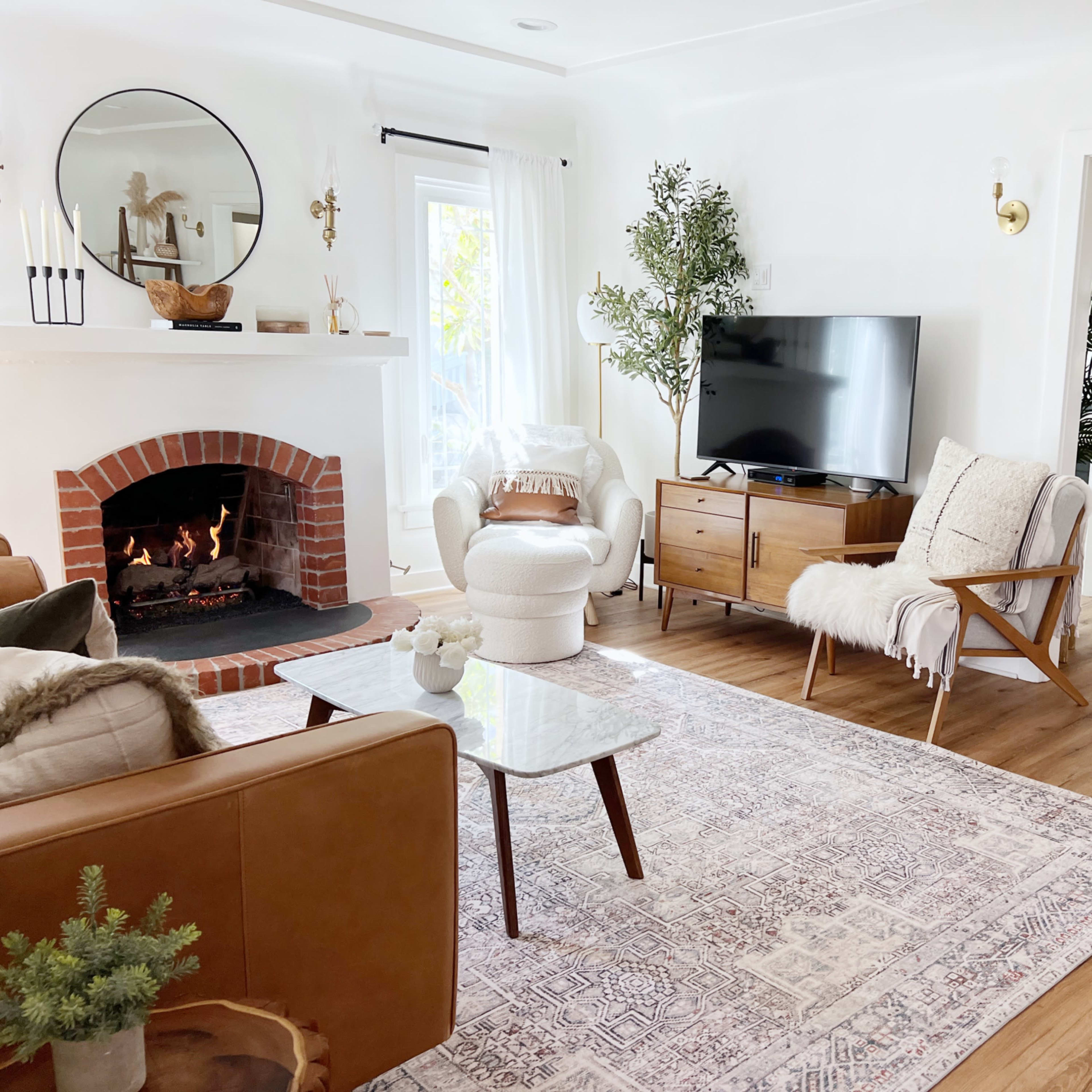 A living room with a fireplace, a television on a wooden cabinet, and a dining area visible in the background.