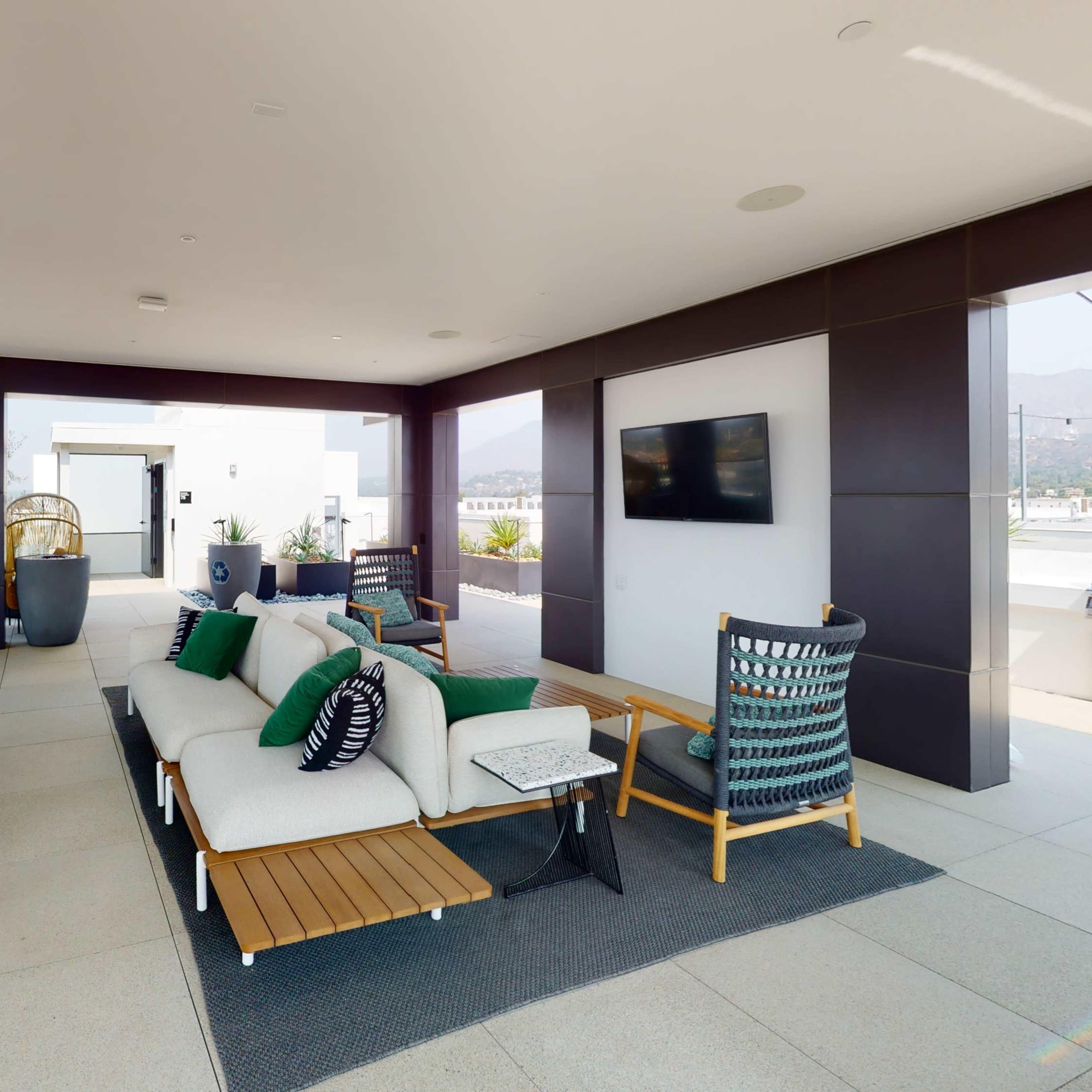 A modern outdoor lounge area featuring a pool table, a sectional sofa, and a grill station, overlooking a cityscape.