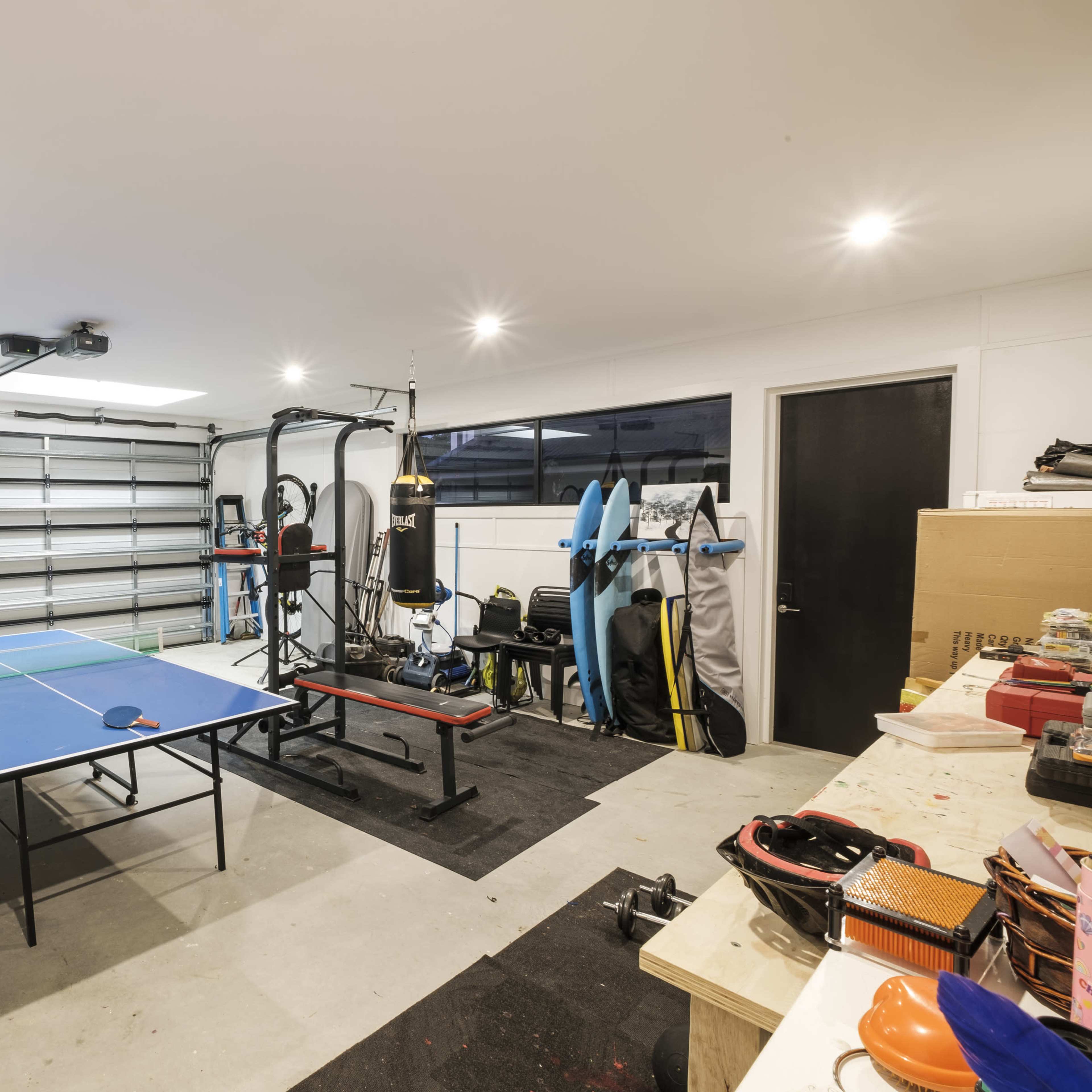 A spacious garage that features a ping pong table, exercise equipment, and various storage items along the walls.