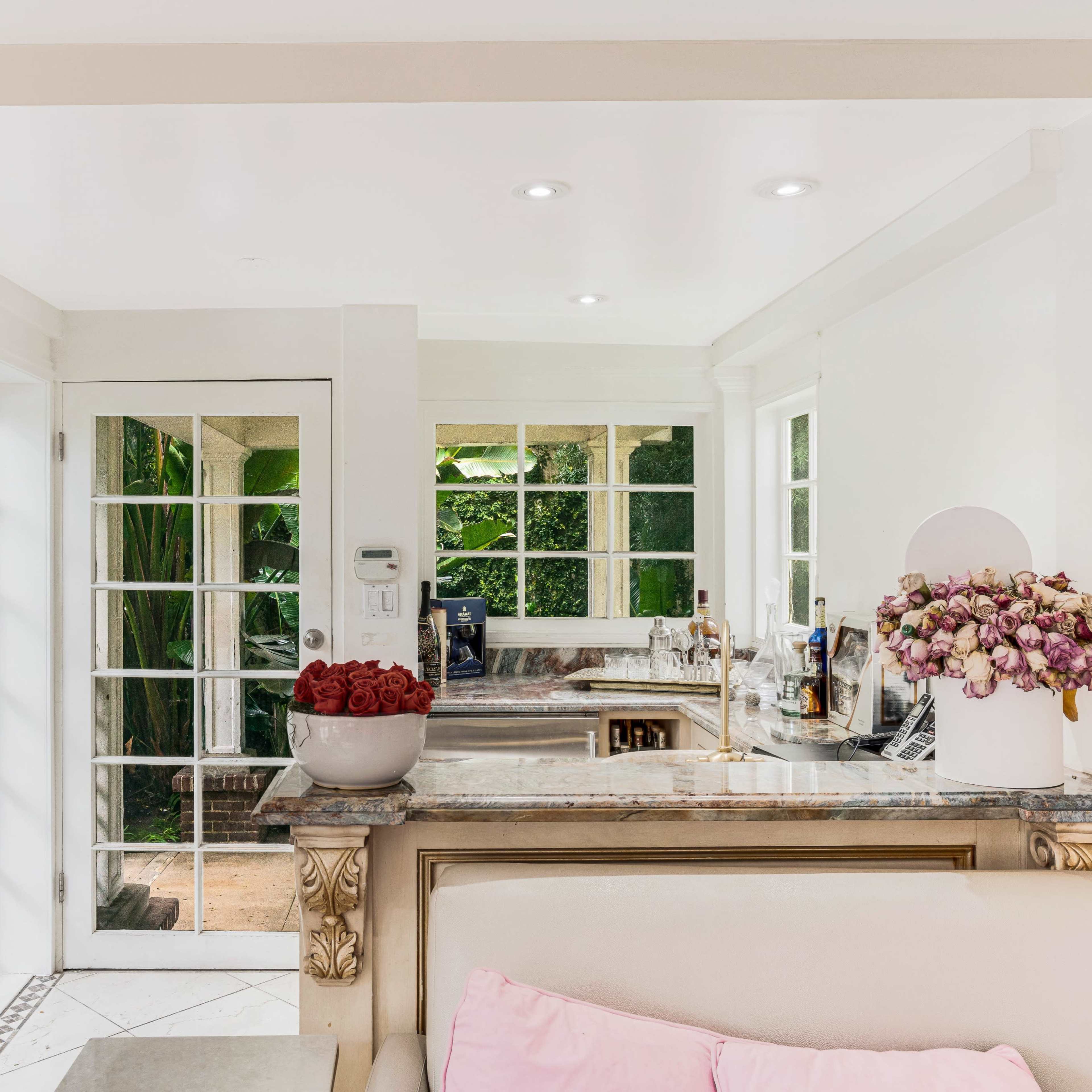 A well-lit kitchen features marble countertops, glass door access to an outdoor space, and decorative flowers on the counter.