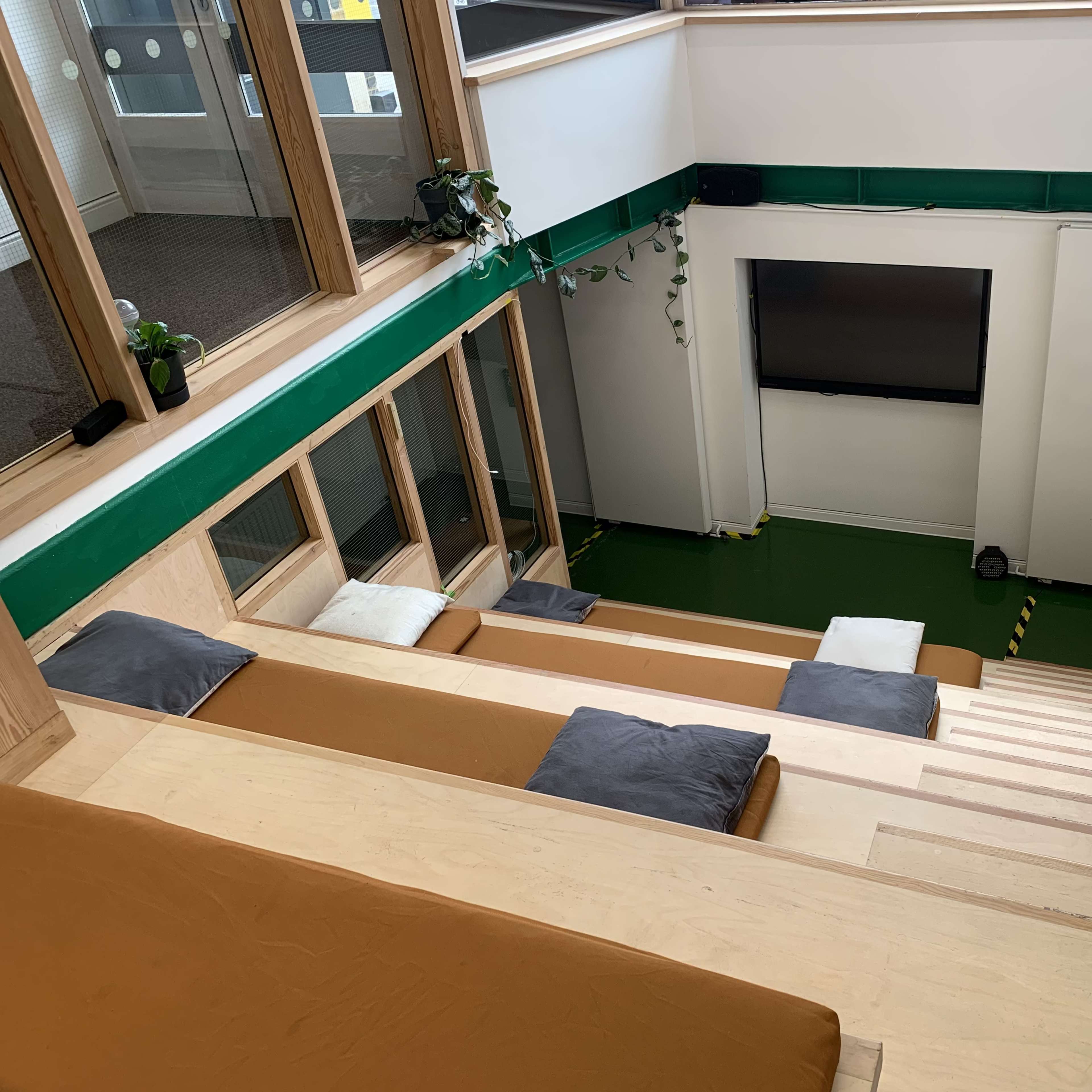 A modern indoor staircase leading down to a green floor area with a large screen at the bottom and seating arrangements along the sides.