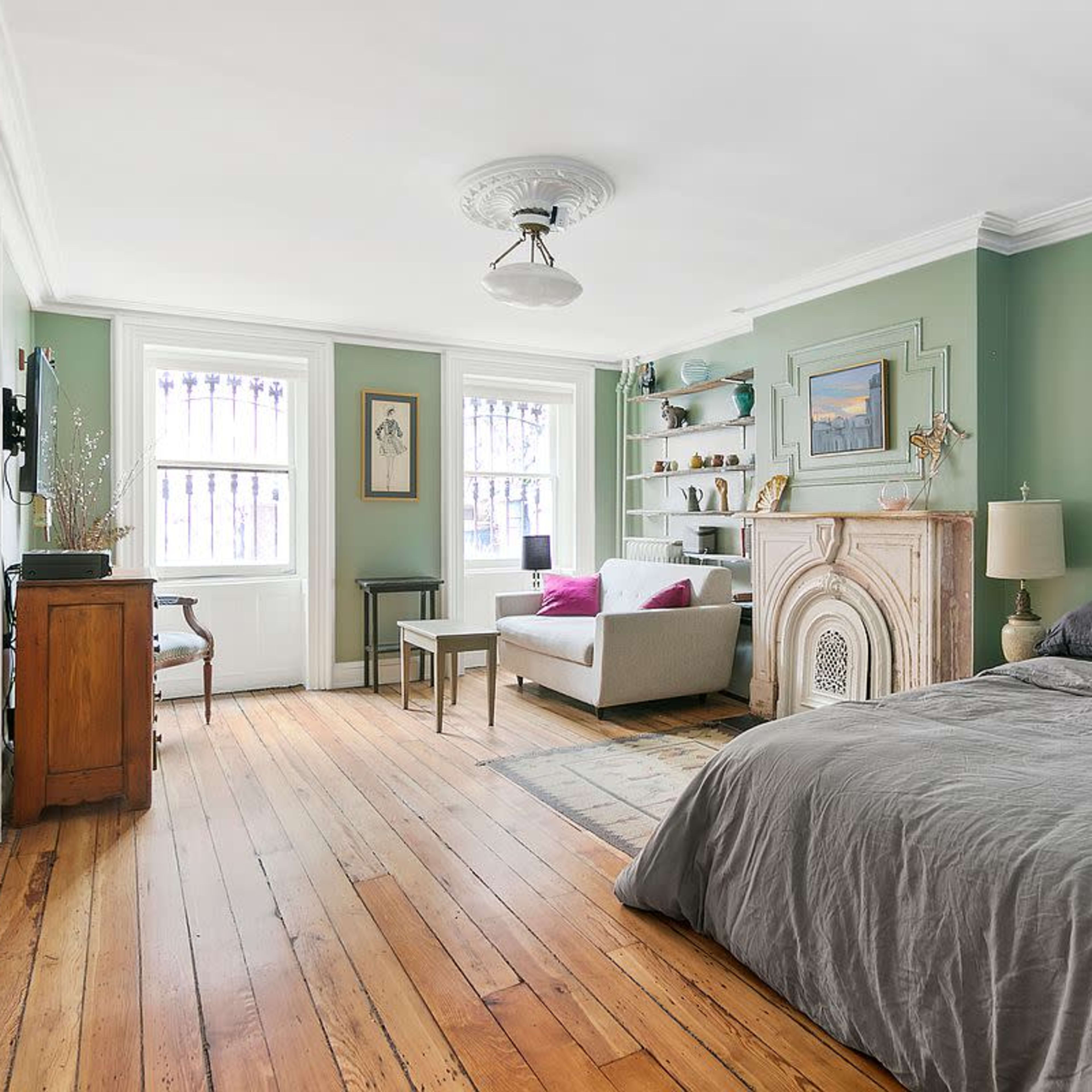 The room features a bed with gray bedding, a wooden floor, a fireplace decoration, and a seating area with a sofa and a small table.