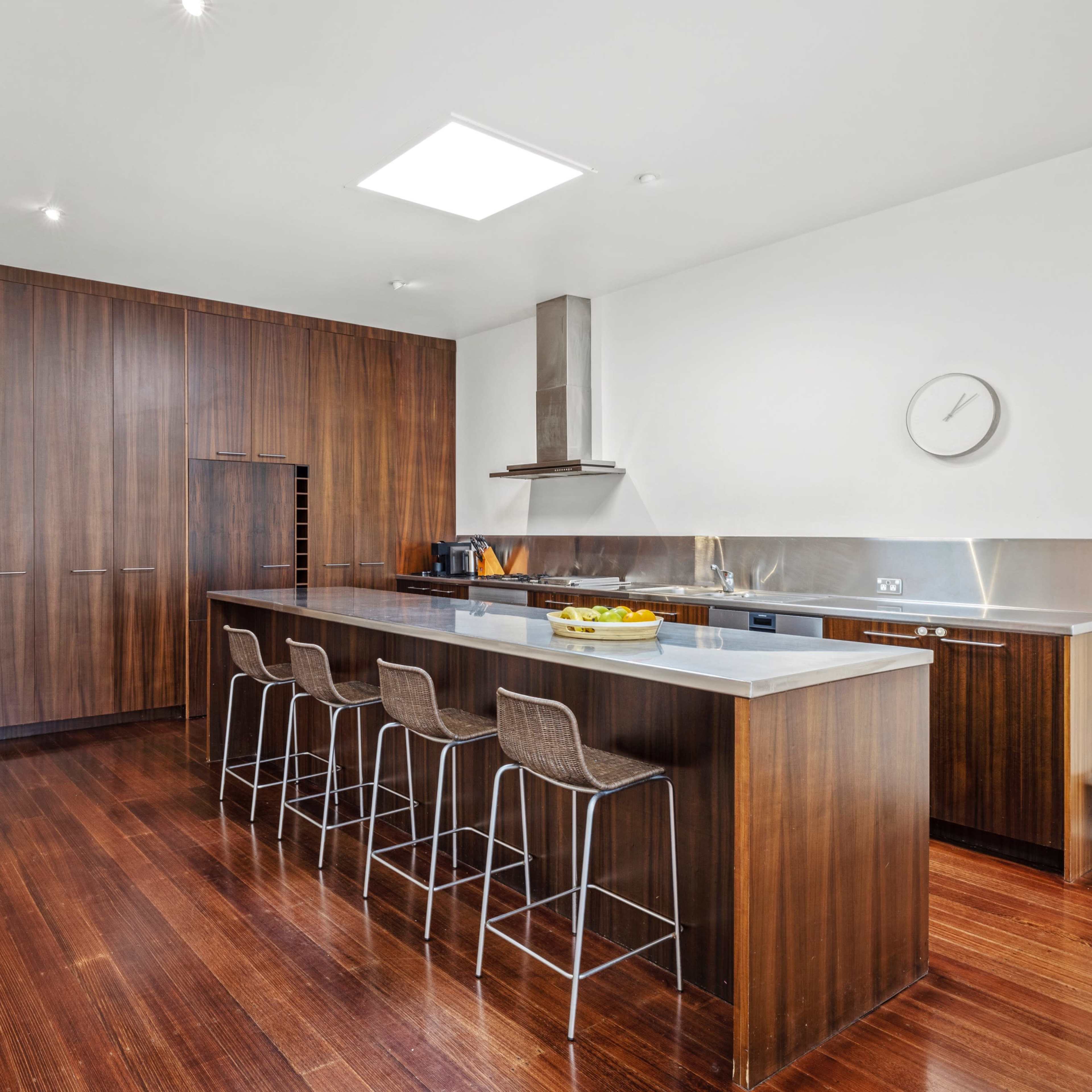 A modern kitchen featuring dark wooden cabinetry, a central island with bar stools, and sleek stainless steel appliances.