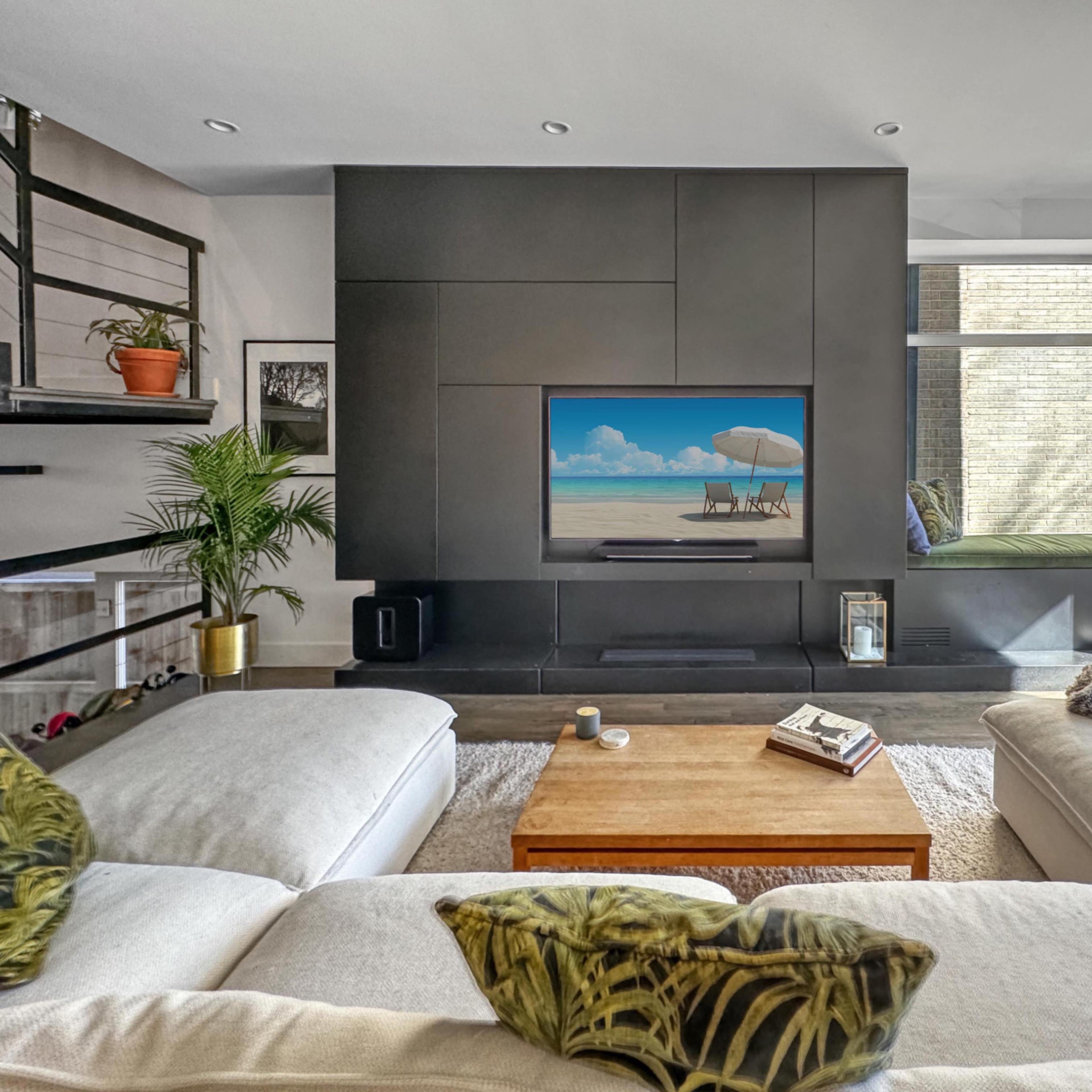 A modern living room features a large sectional sofa, a wooden coffee table, and a wall-mounted television displaying a beach scene.