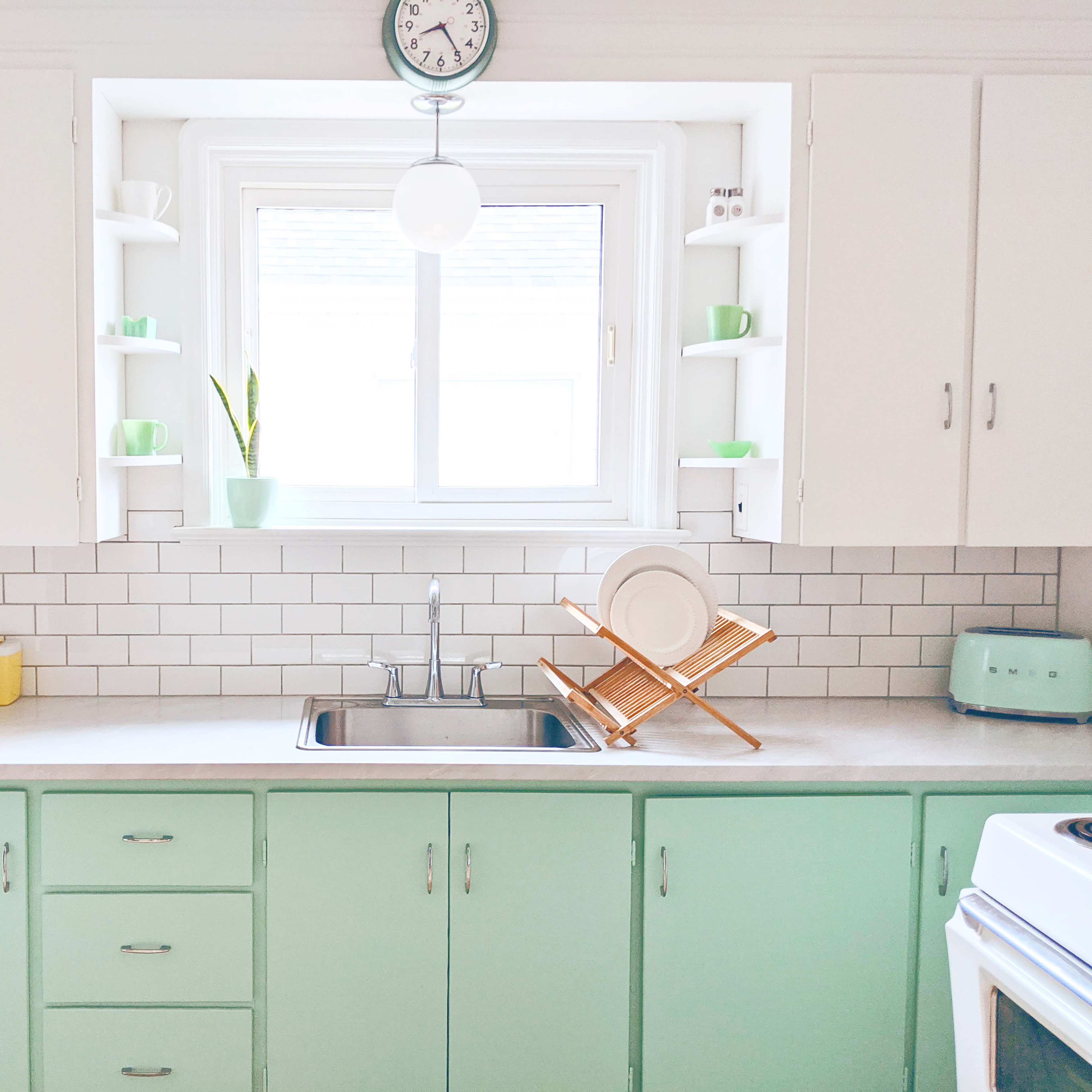 A bright kitchen featuring mint green cabinets, white countertops, and a window over the sink with dishes drying on a wooden rack.