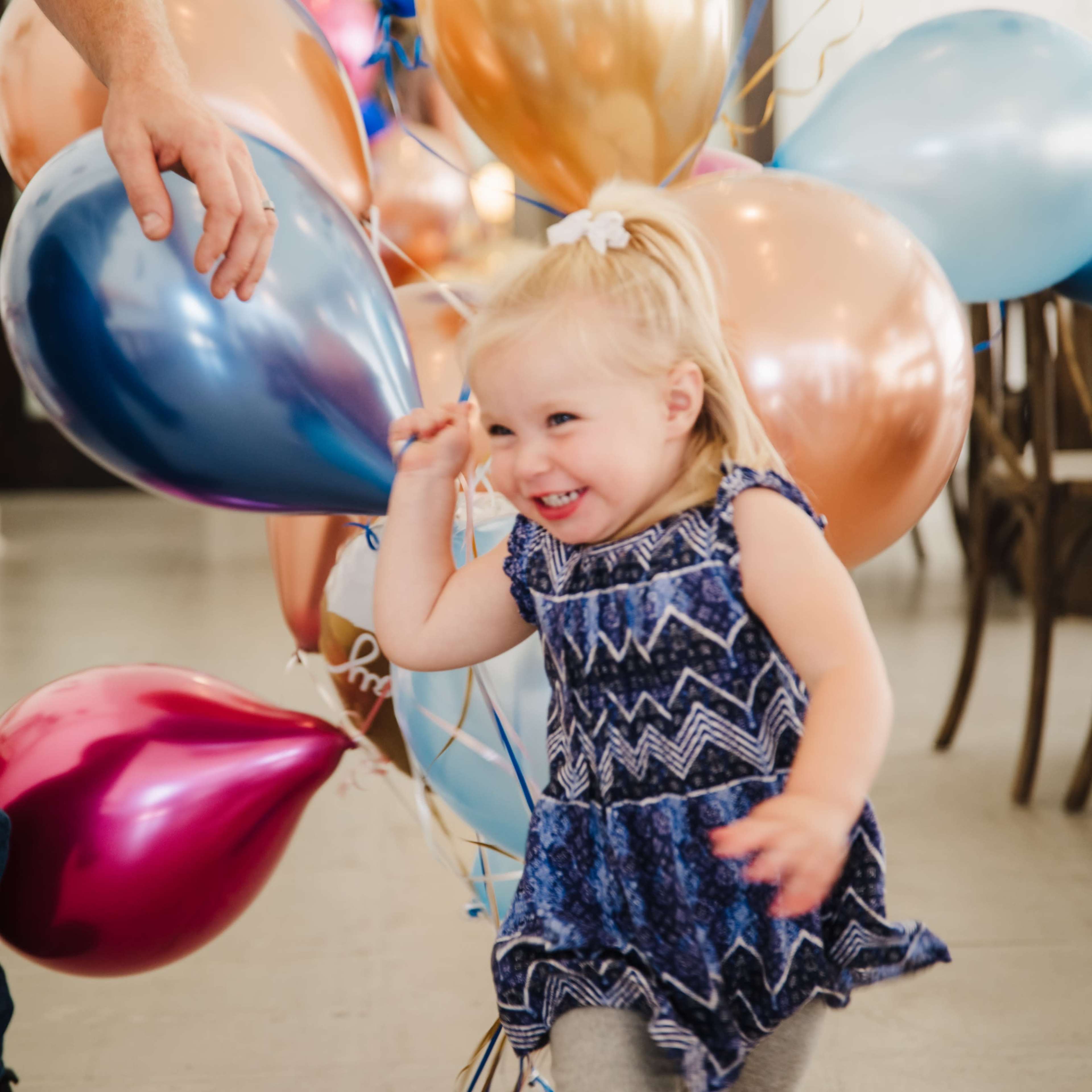 A small child runs joyfully among colorful balloons at a celebration.