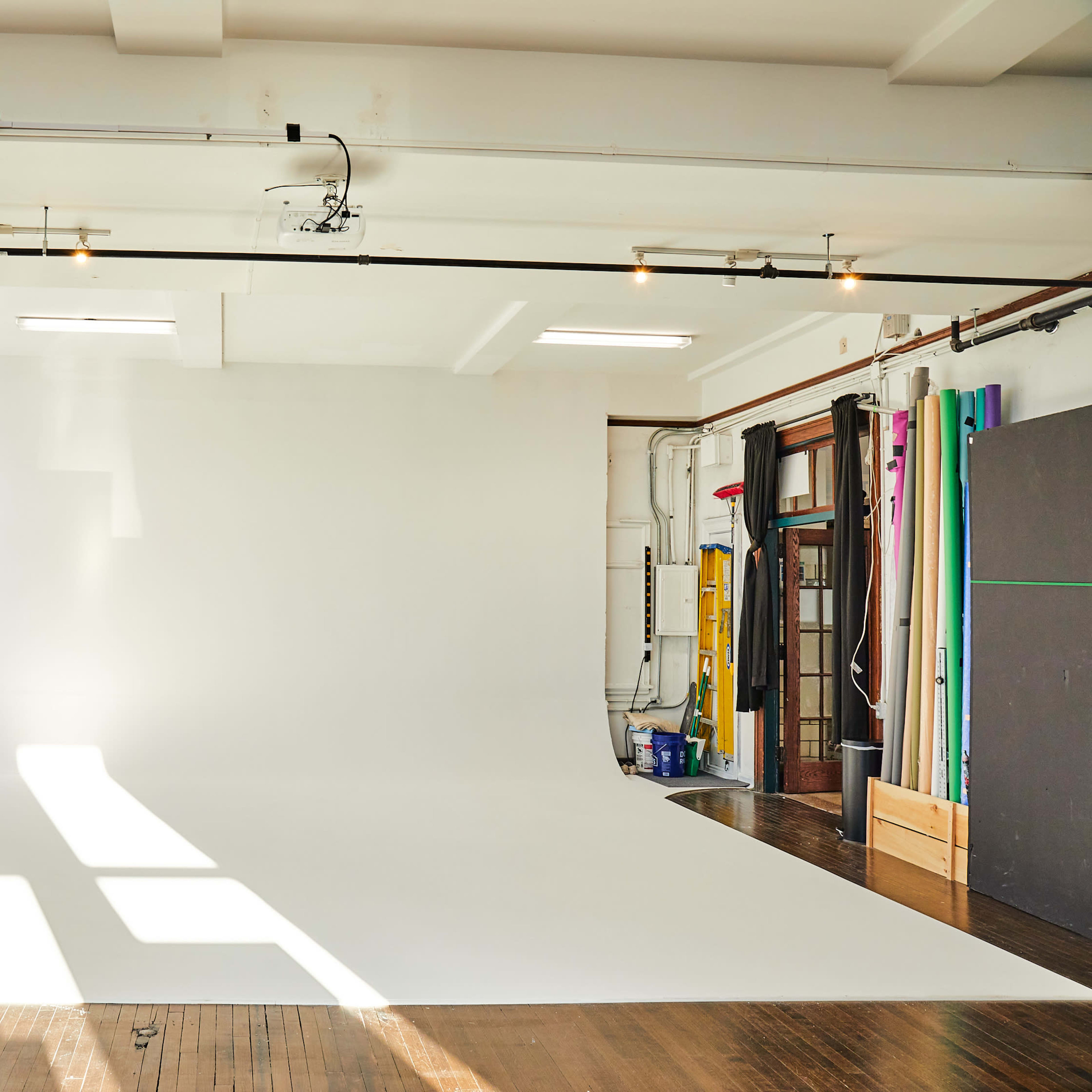 A bright photography studio with a large white backdrop, natural light coming through the windows, and various equipment set up along the walls.