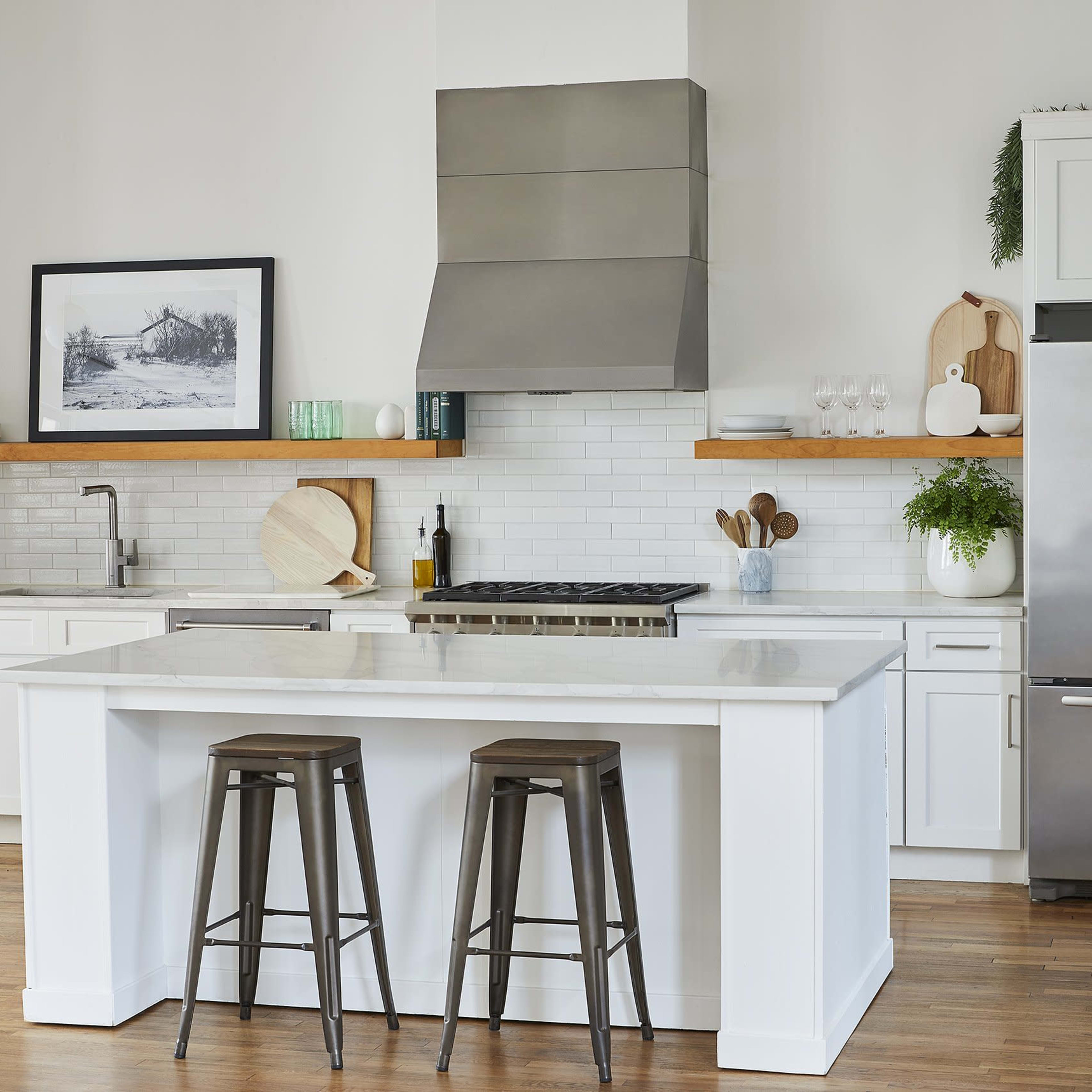 A modern kitchen features white cabinetry, a stainless steel refrigerator, and a central island with two metal stools.