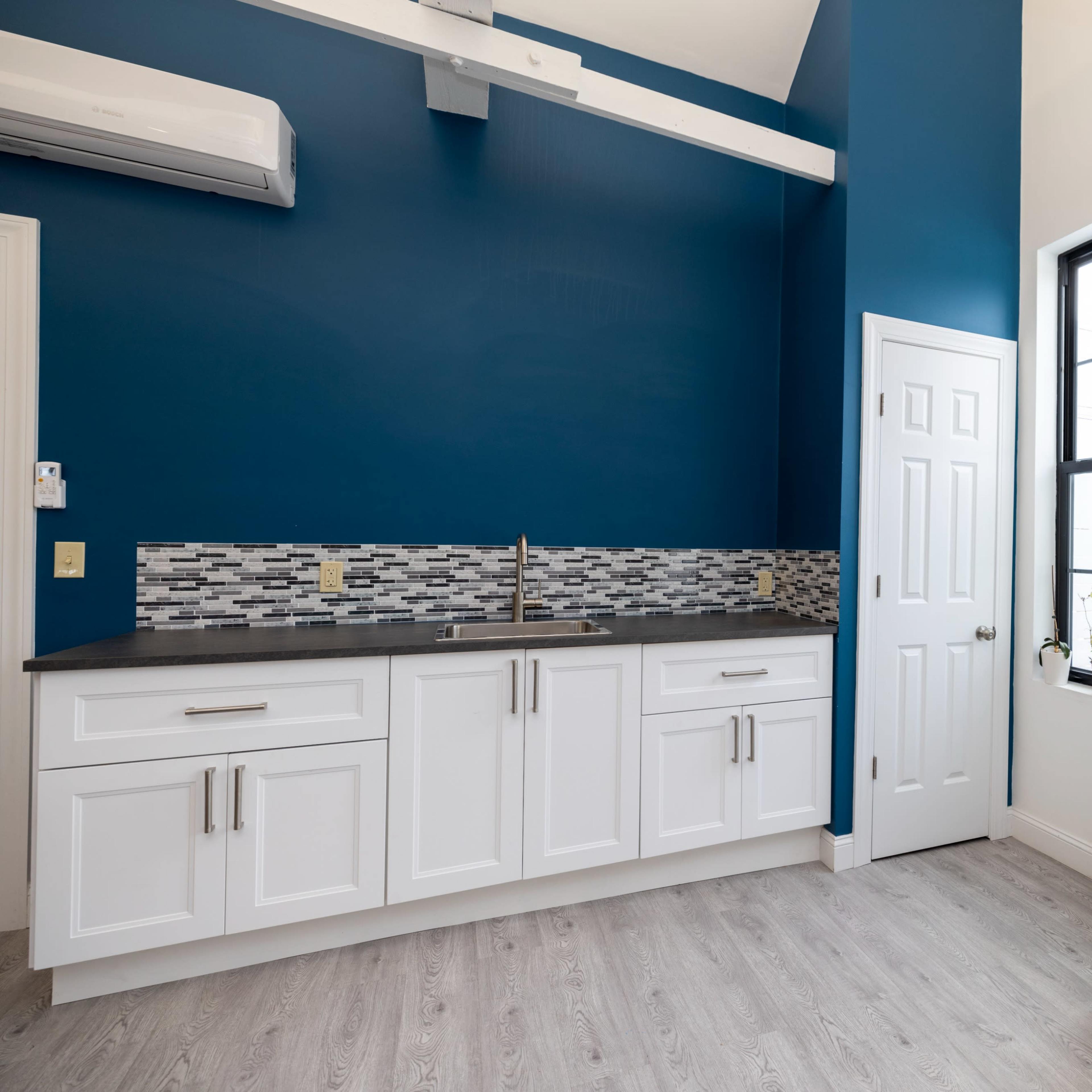 A kitchen with white cabinetry, a dark countertop, and a blue accent wall, featuring a stainless steel backsplash and a large white refrigerator.