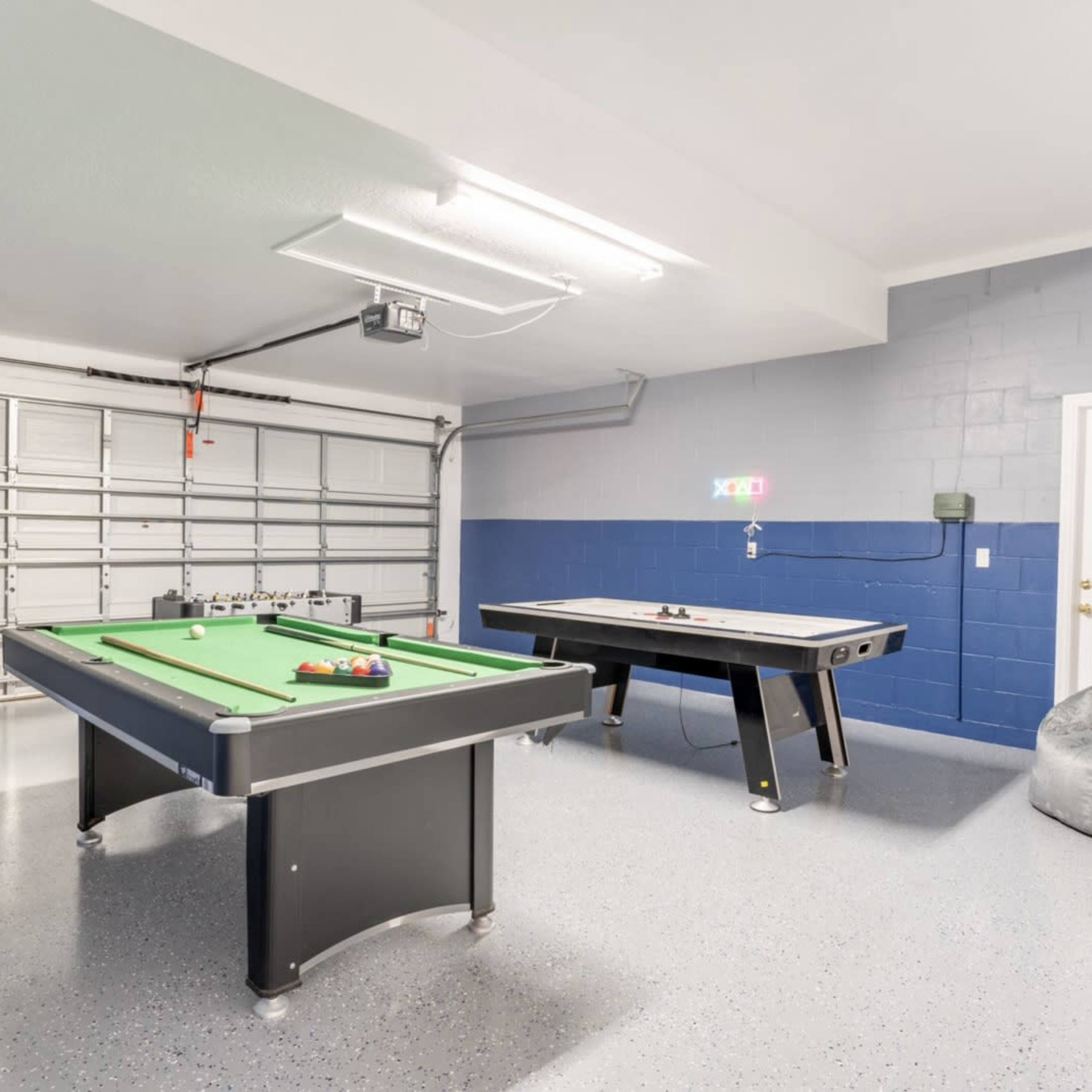 A garage with a green pool table and a black air hockey table, surrounded by bean bag chairs.