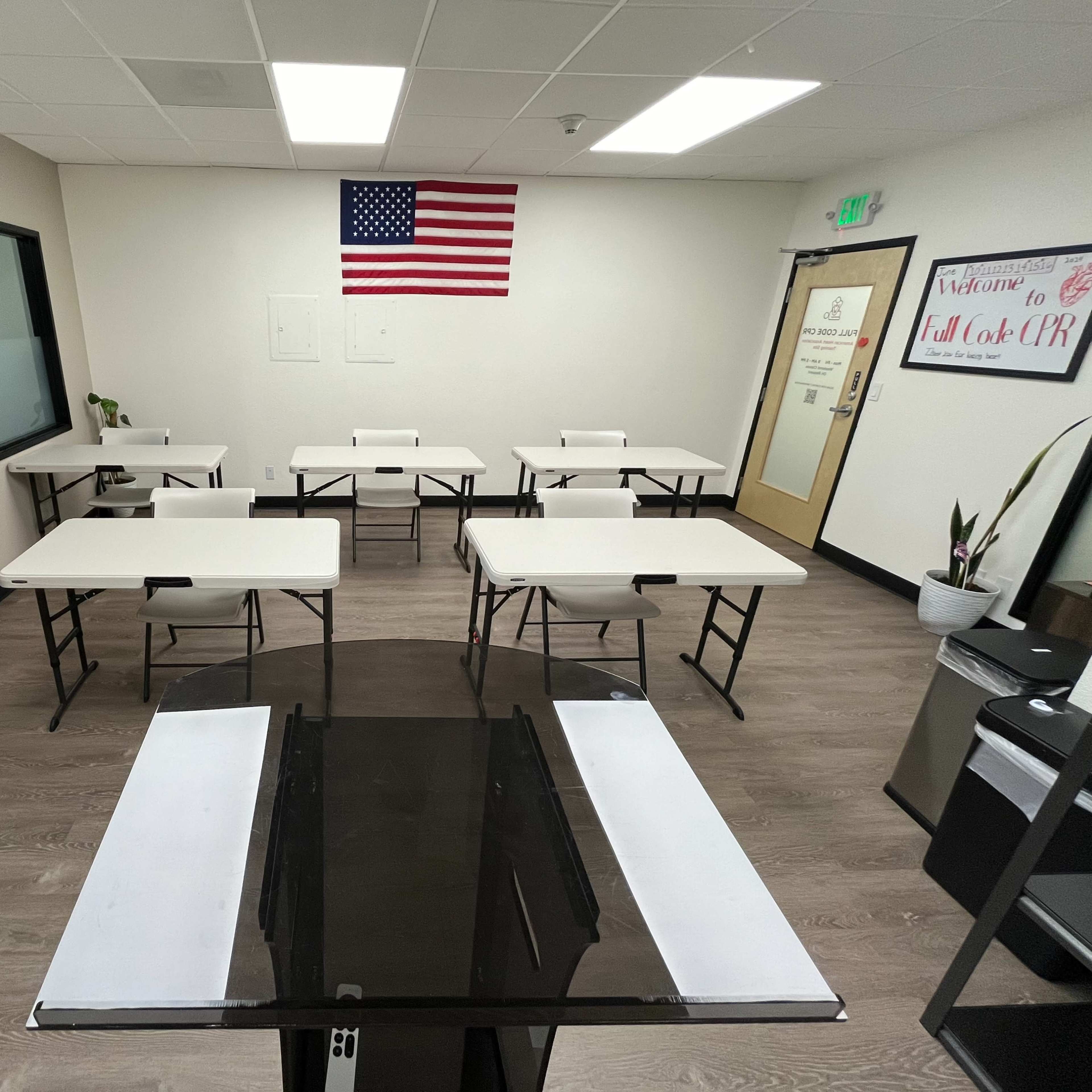 A classroom is set up with multiple tables and an American flag mounted on the wall.