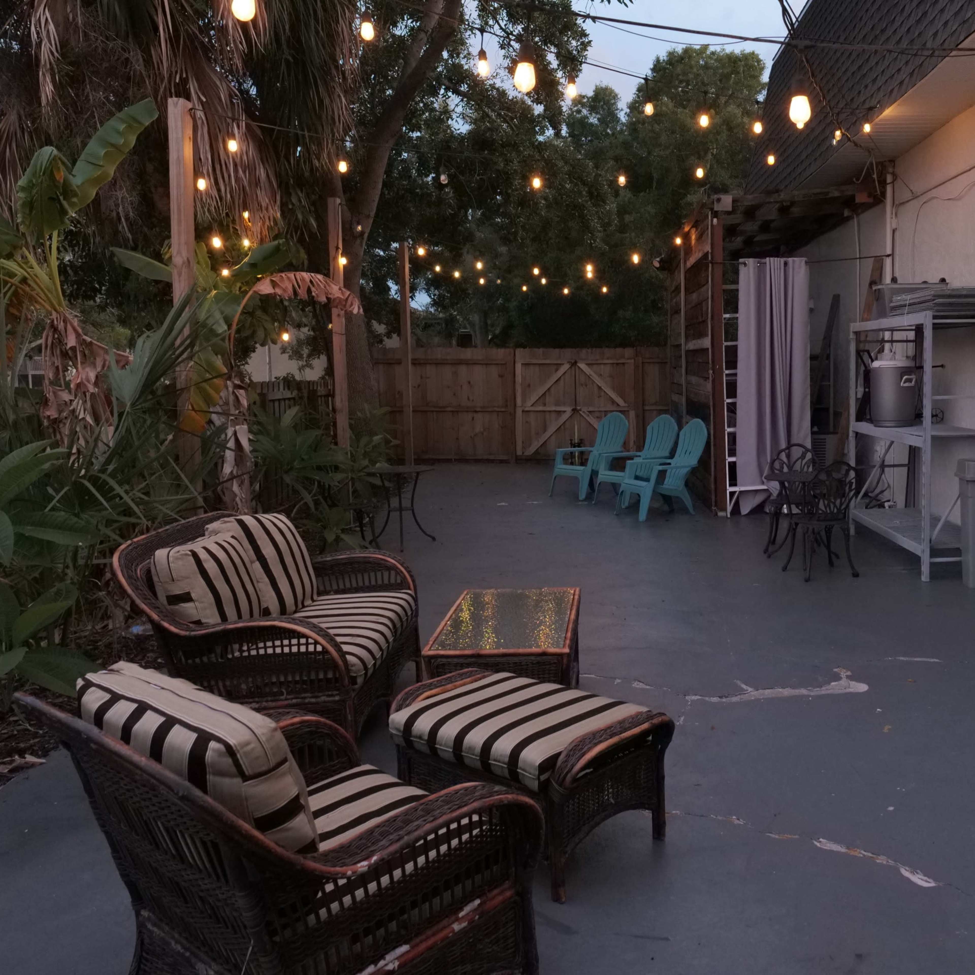 A patio area with string lights overhead, featuring a seating arrangement of wicker chairs and a small table on a concrete surface.