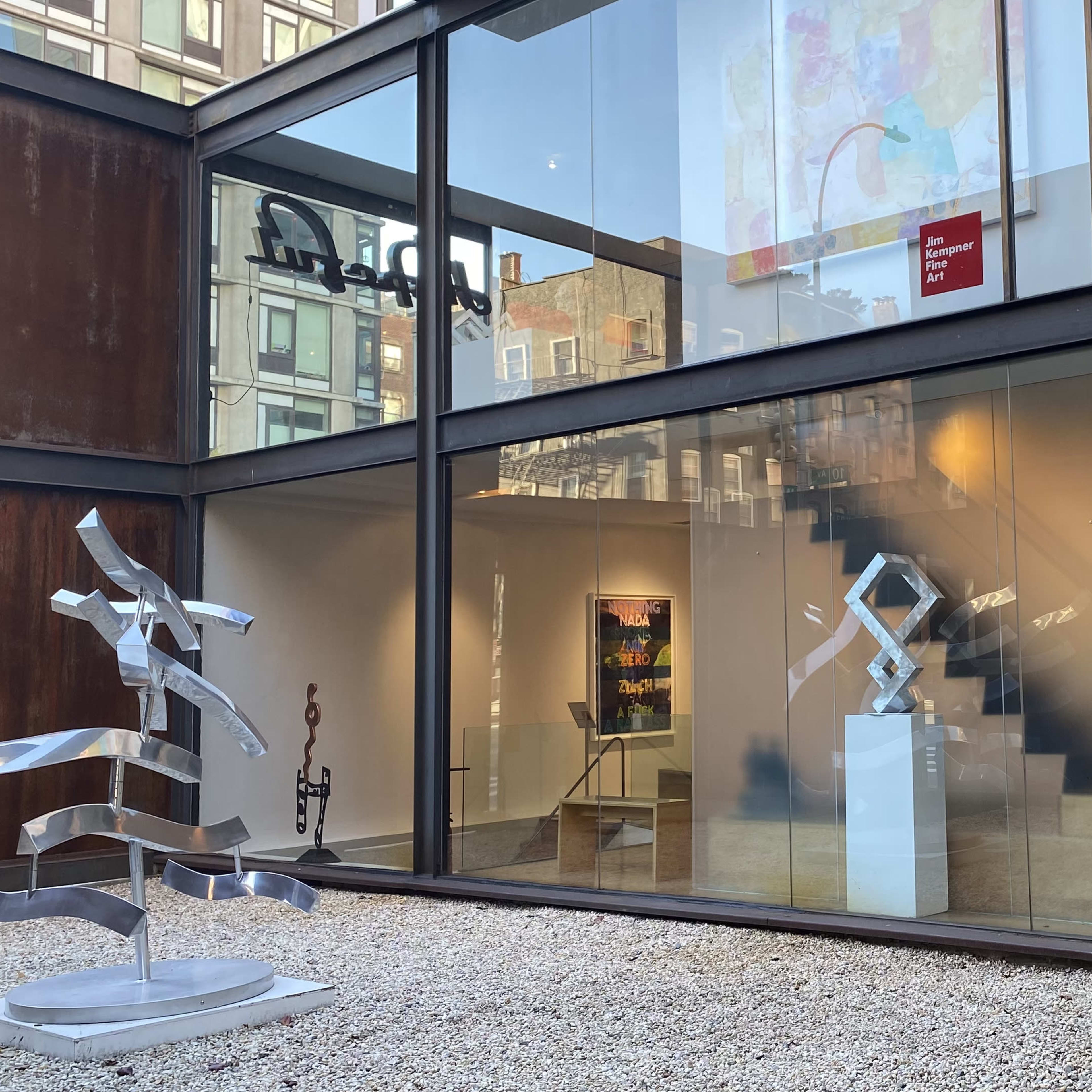 A modern art gallery featuring a glass facade, a staircase, and a sculpture displayed in the outdoor area.