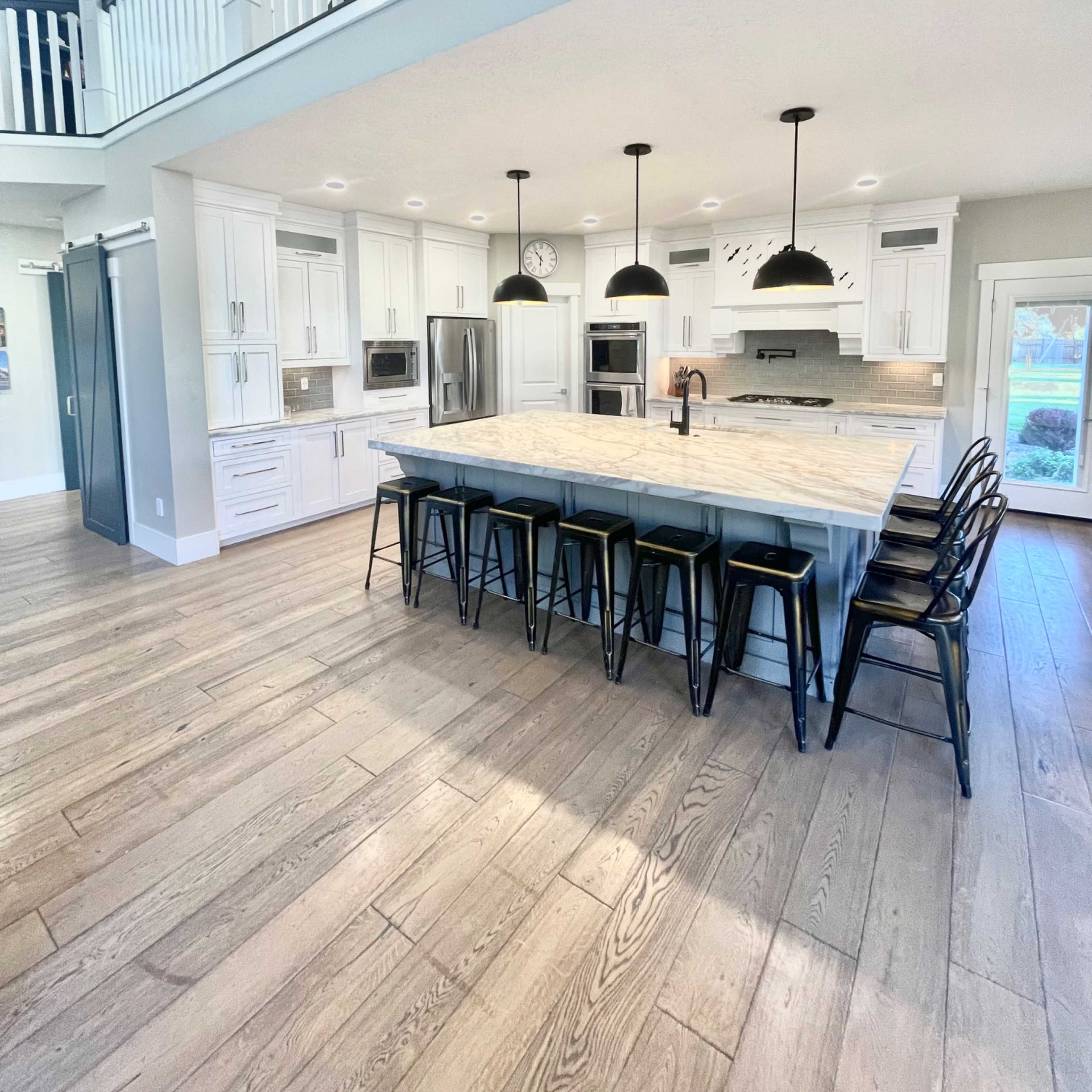 A spacious kitchen features a large island with black bar stools, white cabinets, and modern appliances.